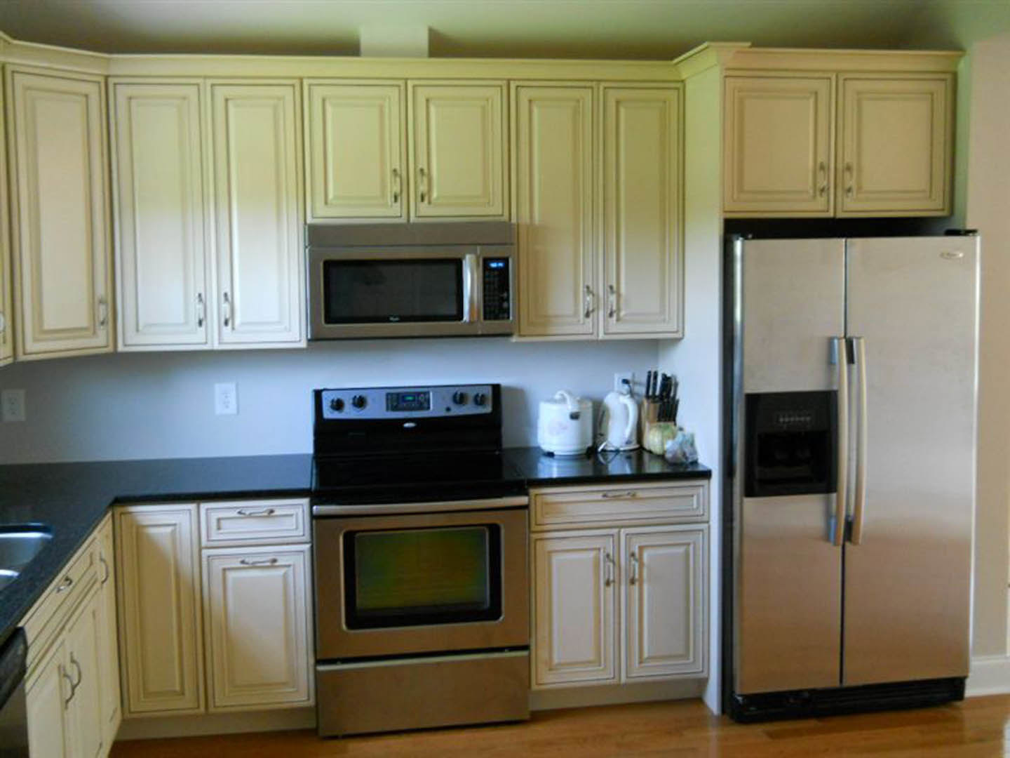 White kitchen cabinets with black countertops, stainless steel refrigerator, open microwave door, white teapot and bowl on counter