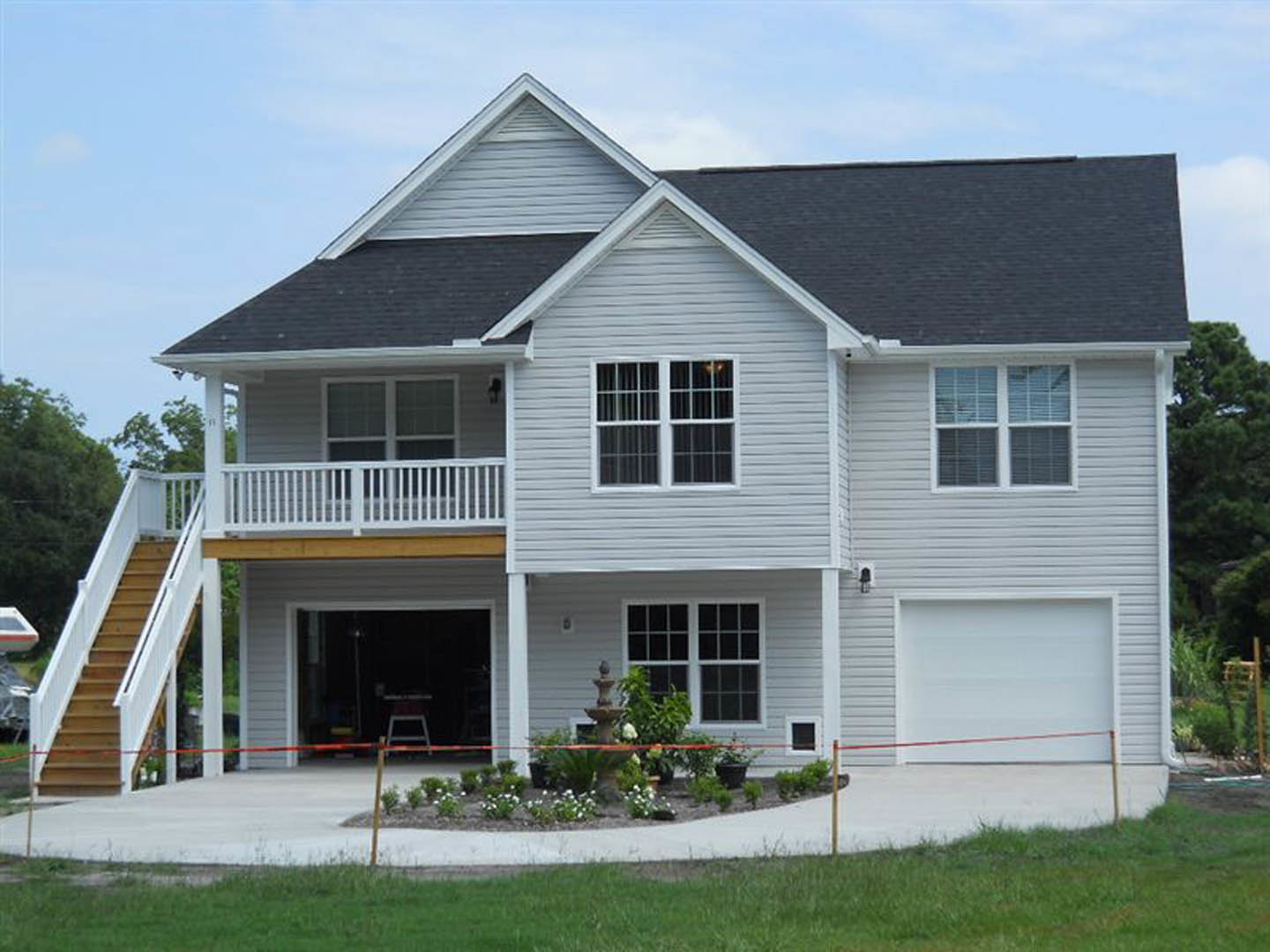 Two-story home with white siding, attached garage, covered front porch, multi-pane windows, landscaped yard with green grass and shrubs