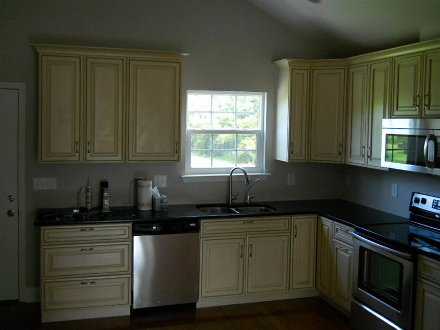 White kitchen cabinets with silver handles, black countertops, built-in microwave oven, multi-pane window, and light-colored walls