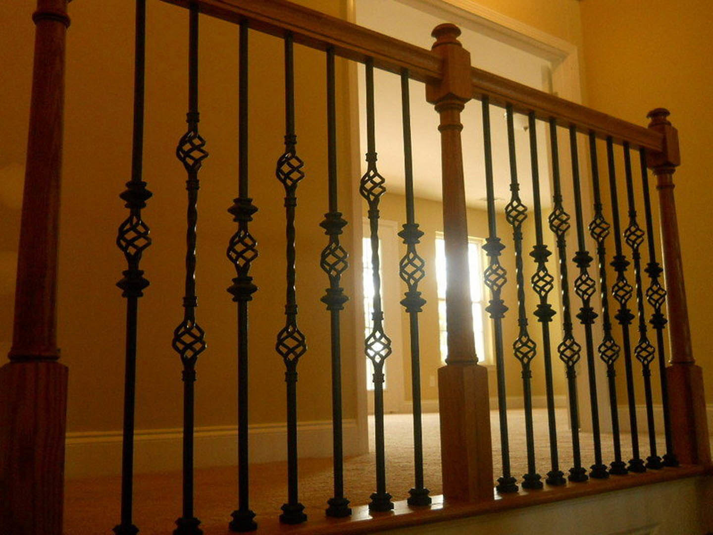 Black iron handrail with wooden post on staircase, set against a yellow wall