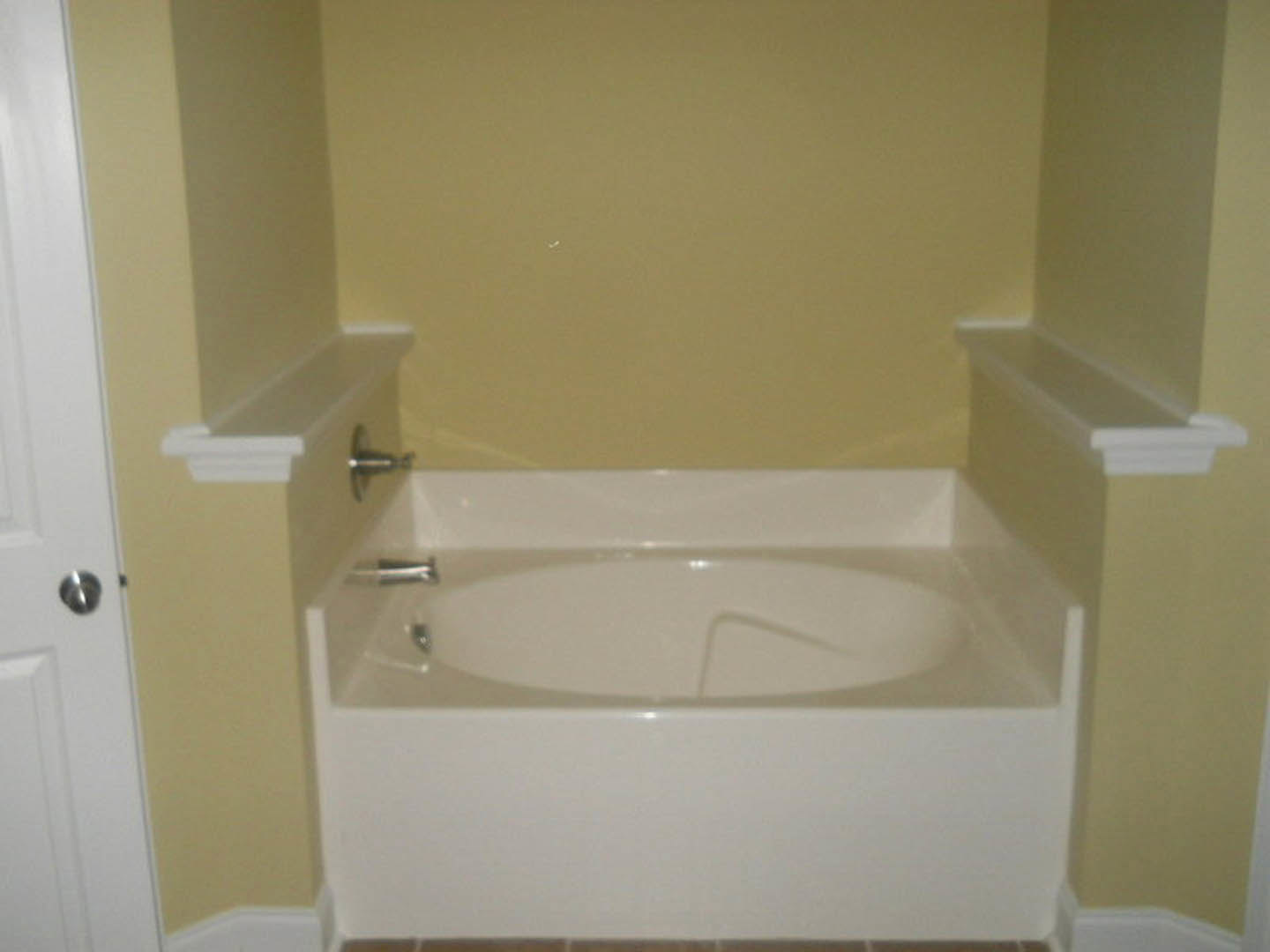 Freestanding white bathtub beside tiled wall, modern chrome faucet, white sink with silver tap, neutral bathroom finishes