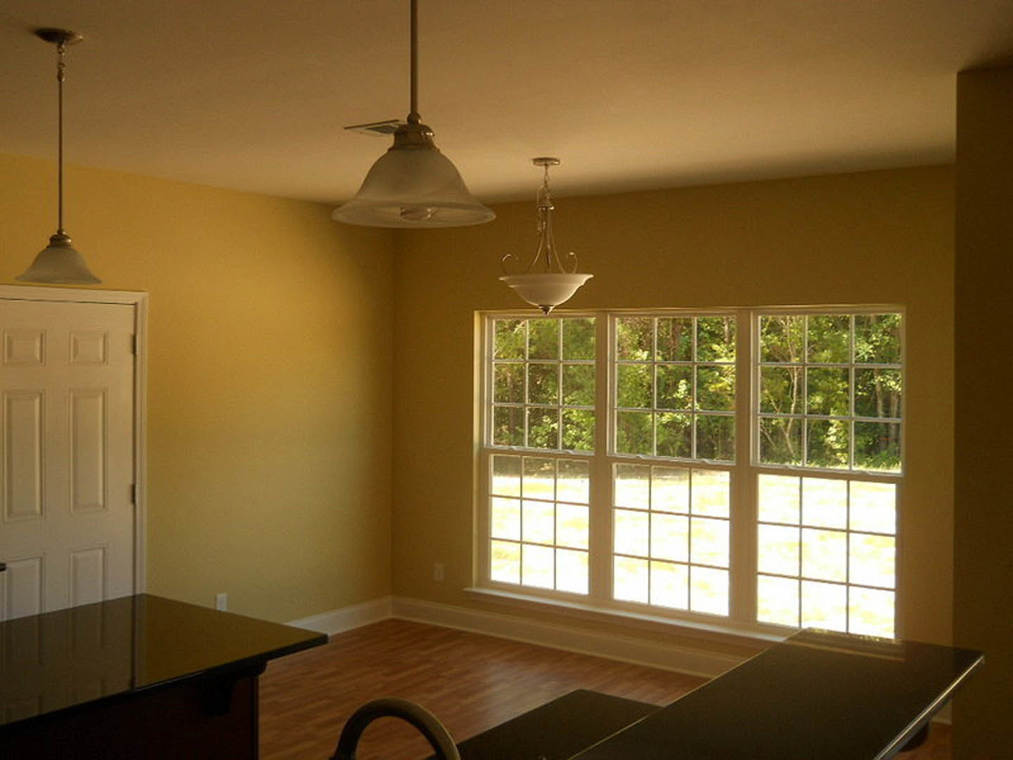 Spacious room featuring a large window with white blinds, light-colored walls, ceiling fan with light fixture, wooden table, and built-in cabinetry.