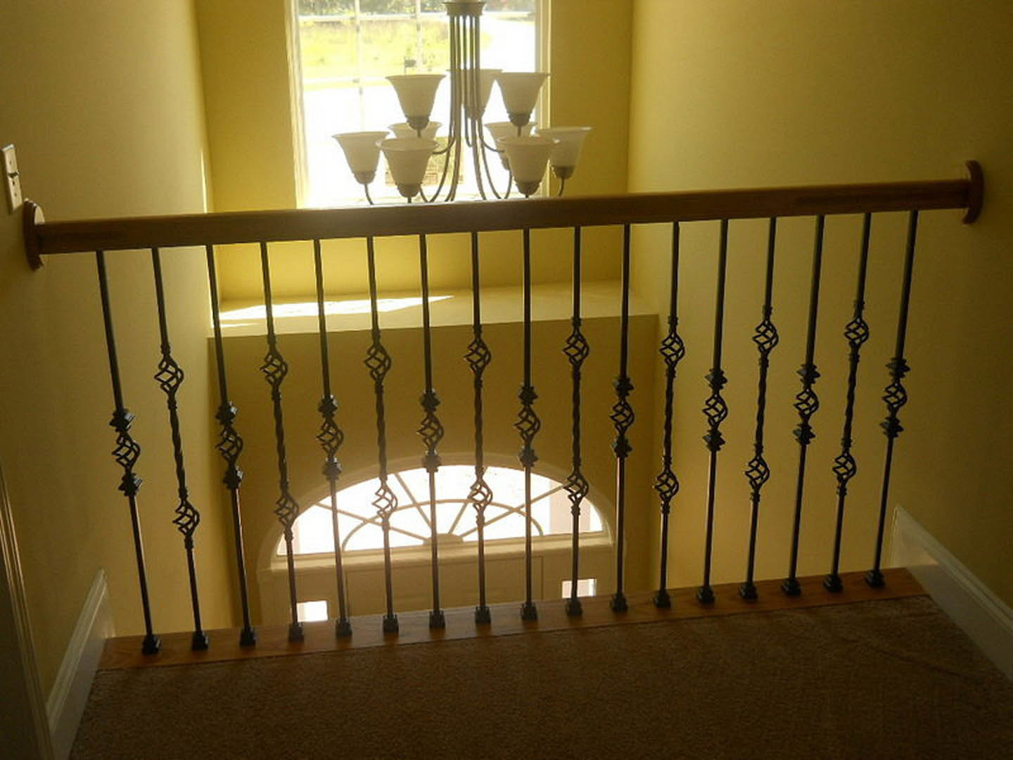 Iron baluster staircase with dark wood handrail, large metal chandelier overhead, neutral walls, and hardwood flooring in a custom home interior