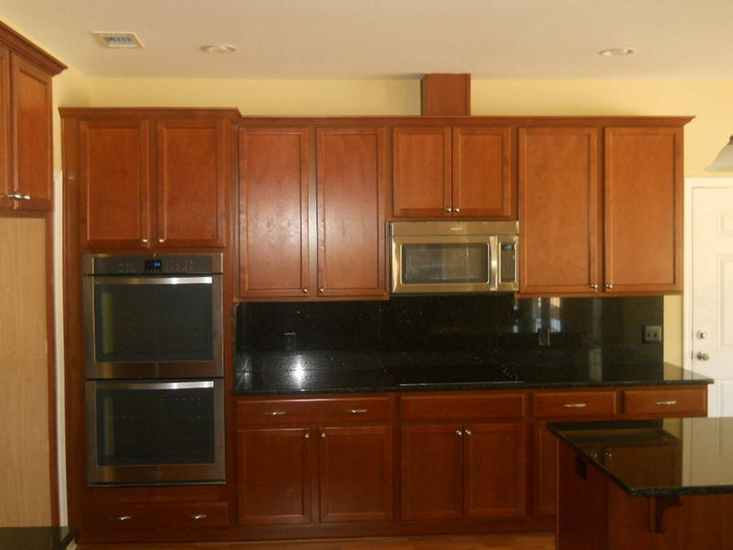 Kitchen with medium-tone wood cabinets, stainless steel microwave and appliances, stone countertop, and neutral painted walls