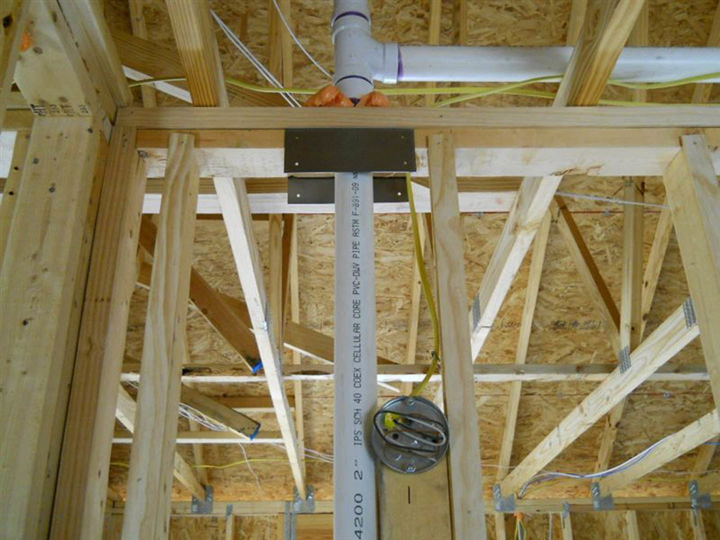 White PVC plumbing pipe installed vertically within unfinished wood framing during home construction.