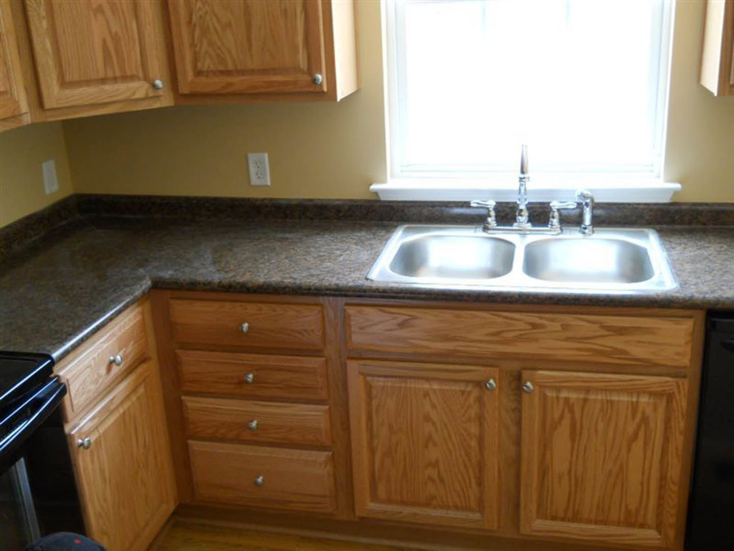 Modern kitchen featuring white shaker cabinets, stainless steel sink with chrome faucet, light quartz countertop, wooden cabinet accents, and a decorative black and white