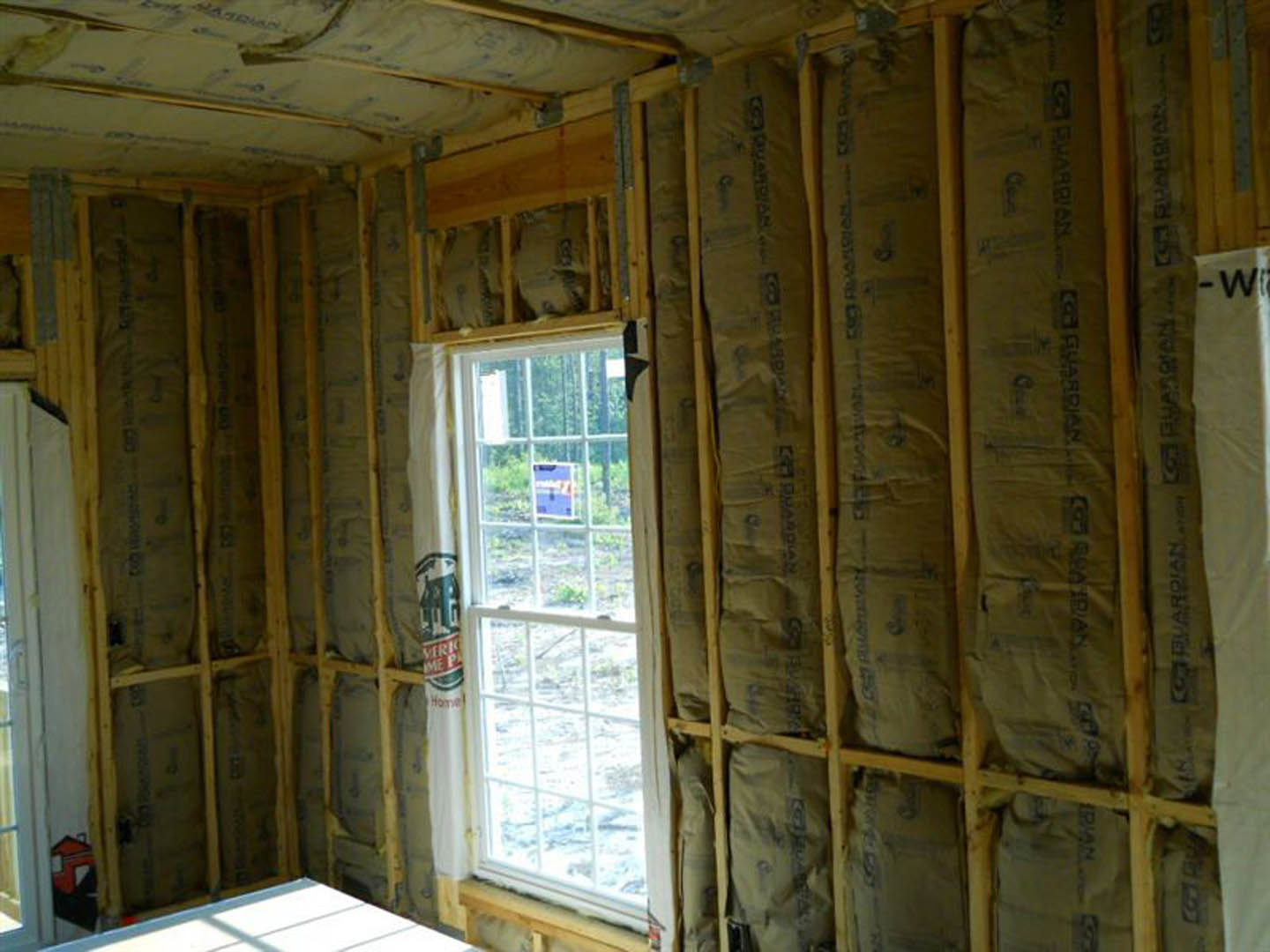 Bright room with two white-framed windows, exposed wood beams, plaster walls, brown bags stacked against one wall, and a close-up view of a wooden door