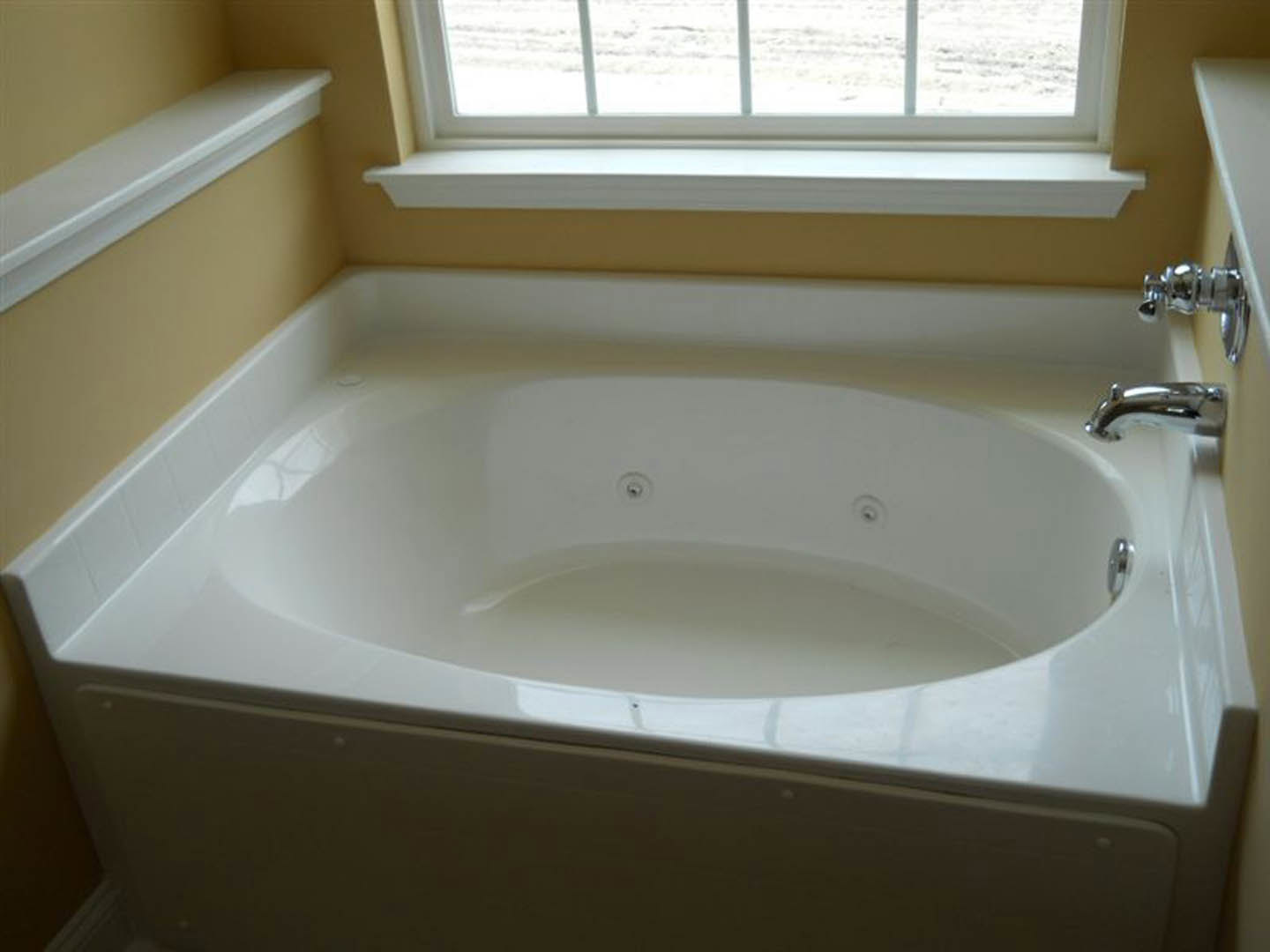 Freestanding white bathtub beneath a large window, white countertop and chrome faucet, bright bathroom with clean finishes
