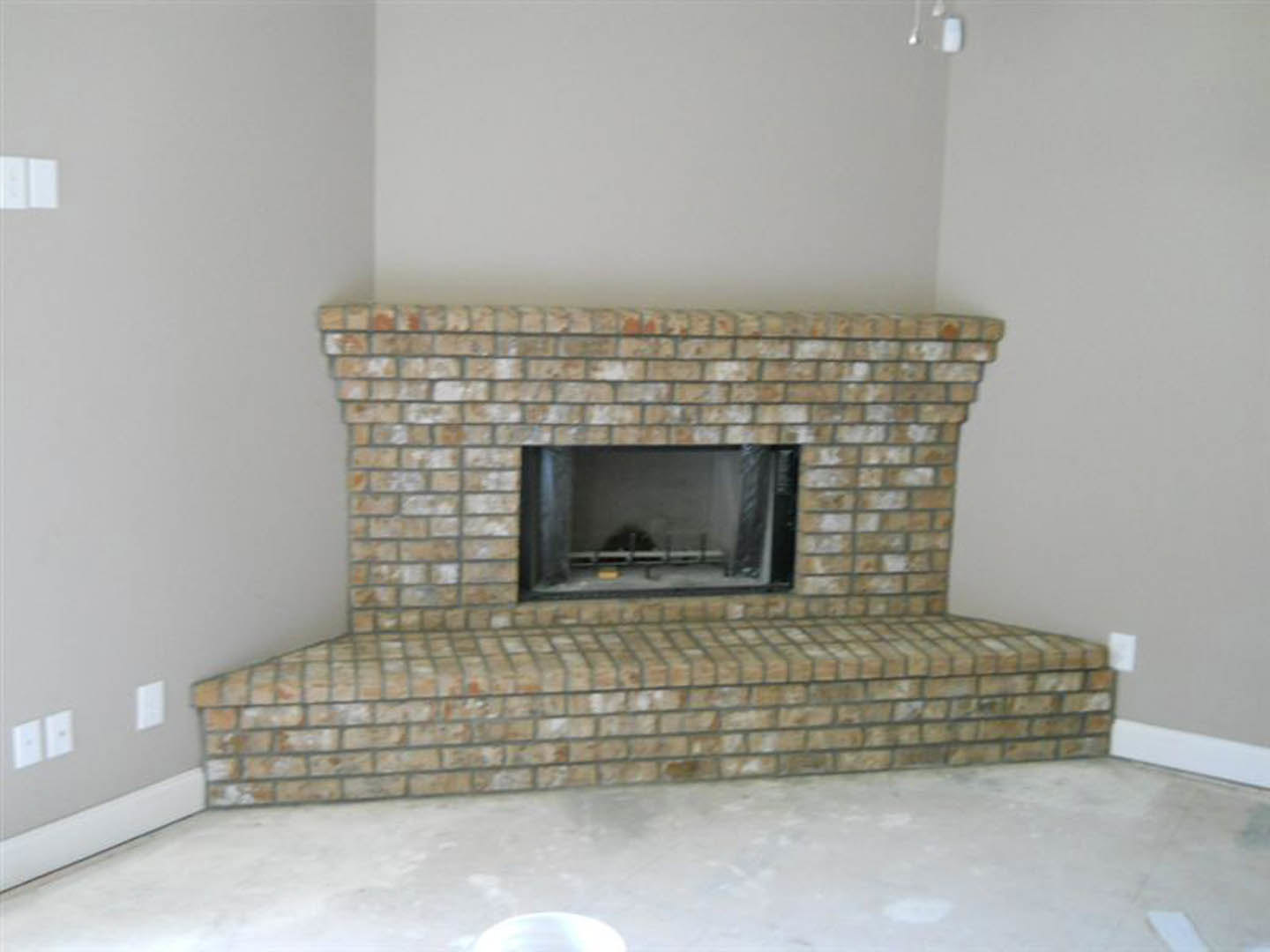 Brick fireplace with stone hearth and fire screen, wood-burning stove, adjacent window, hardwood floor, and neutral walls in a cozy living room.