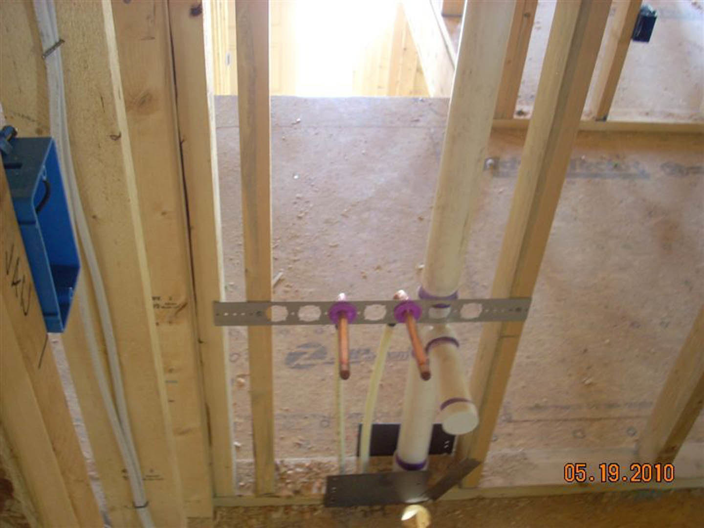 Exposed plumbing pipe with blue insulation, surrounded by unfinished wood framing and construction tools in a residential interior under renovation