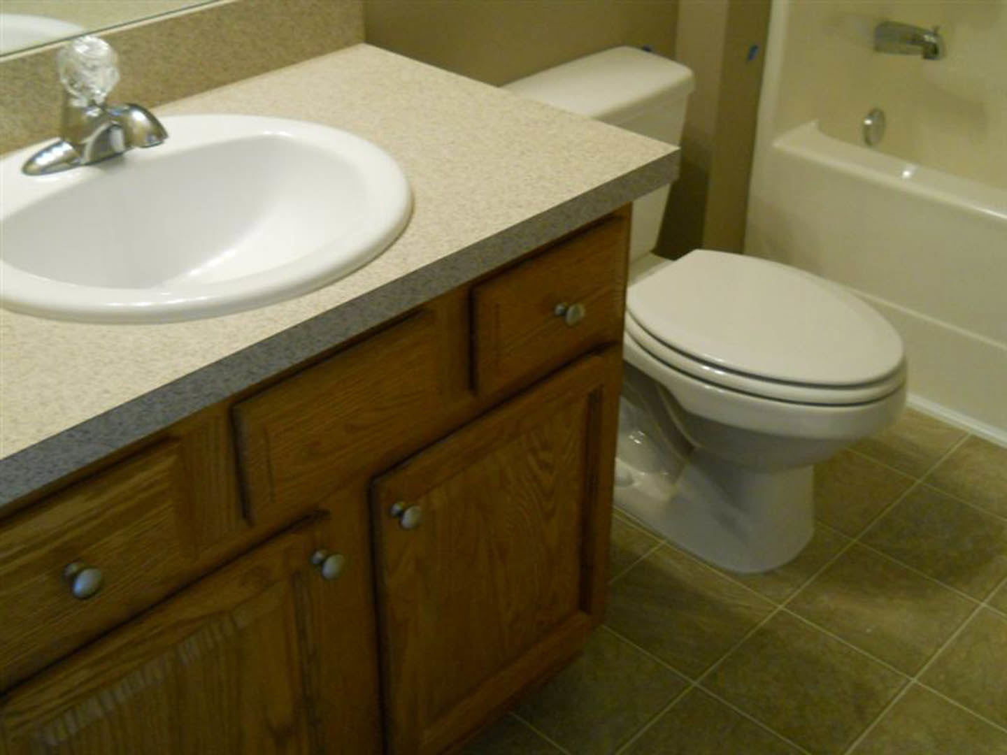 White porcelain sink with chrome faucet beside a closed-lid toilet, set against light tile walls in a modern bathroom.