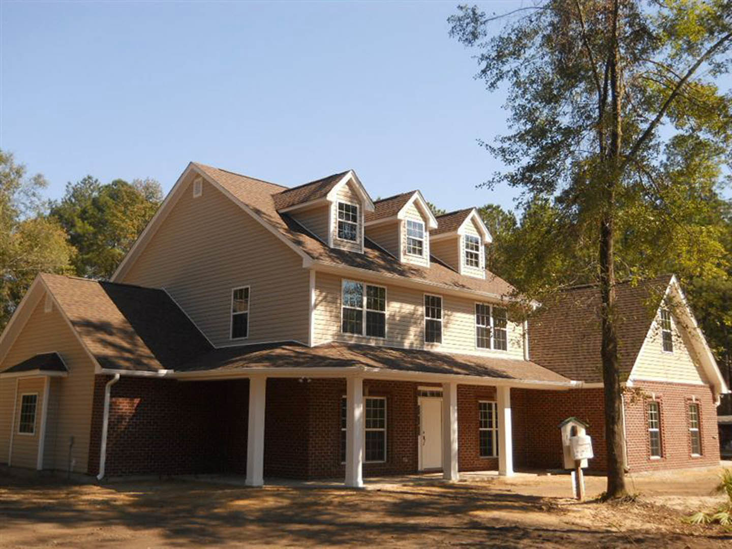 Two-story home with white-framed windows, covered porch, front yard trees, and a mailbox near the walkway