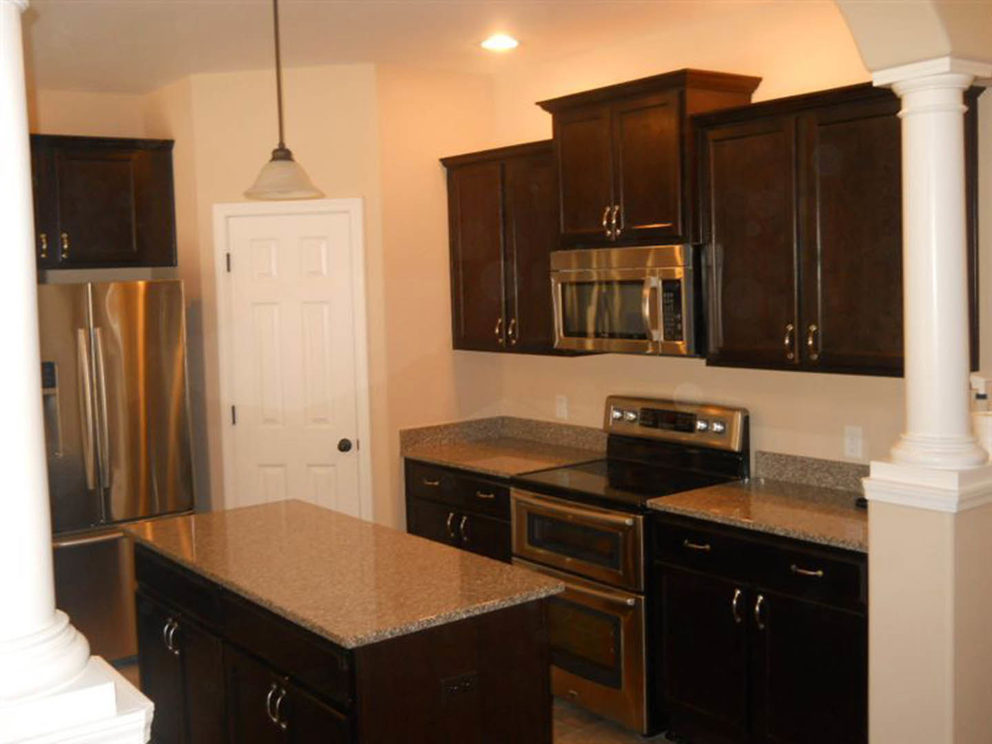 Kitchen with dark wood cabinets, granite countertops, stainless steel appliances, and a white door with black handle