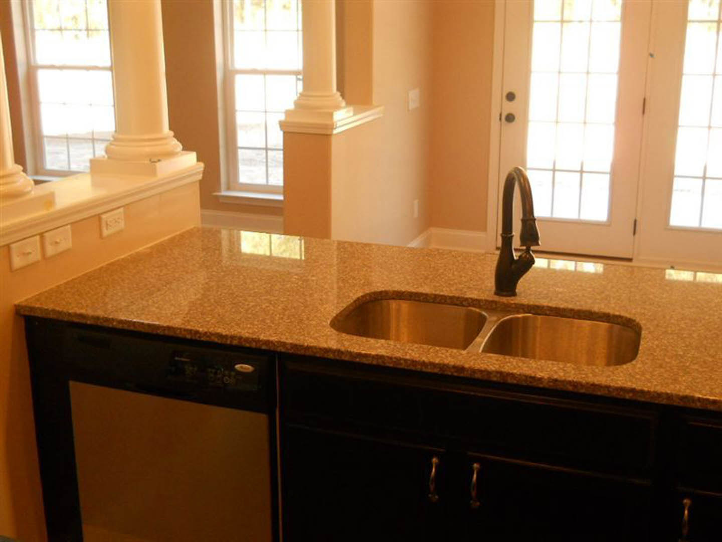 Modern kitchen featuring double stainless steel sinks, built-in dishwasher, white cabinetry, tiled backsplash, and a window above the countertop.