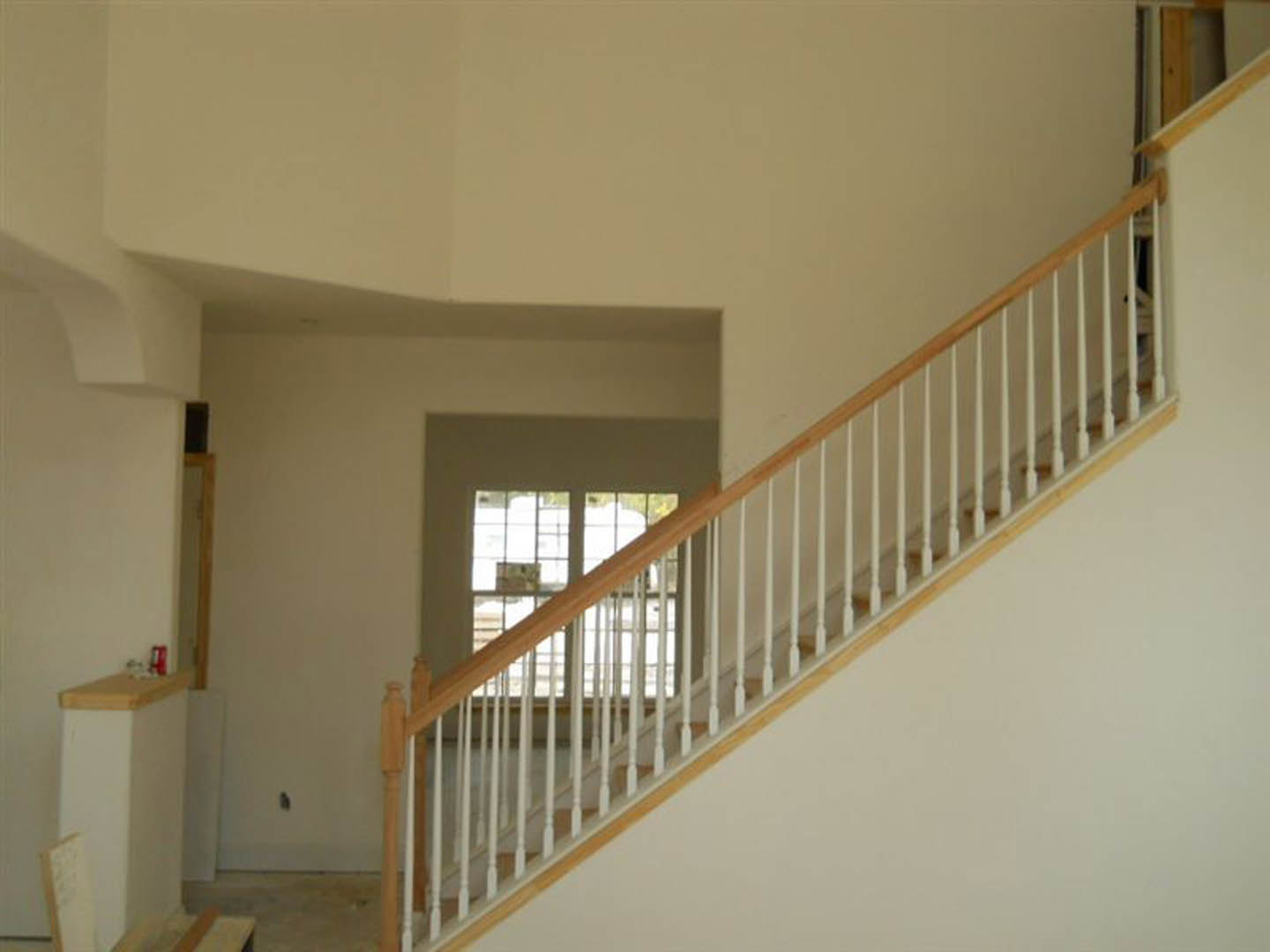 Wood staircase with white balusters and handrail, leading up to a landing with a large window, surrounded by smooth white plaster walls and light hardwood flooring.