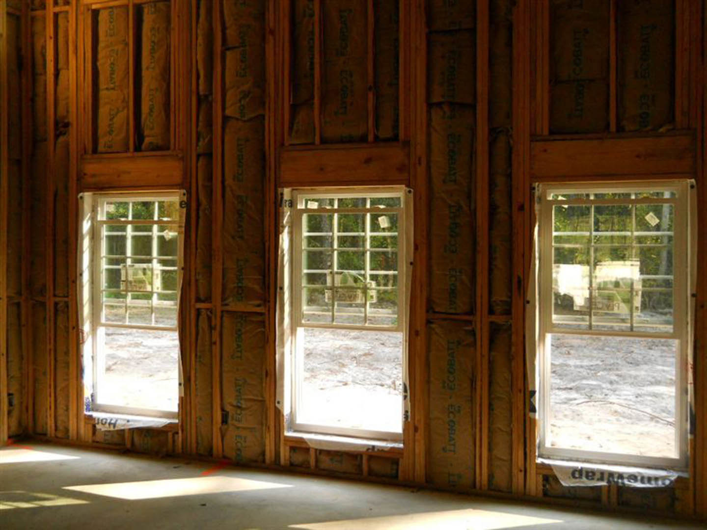 Unfinished room with exposed insulation, wood framing, and multiple white-framed windows showing outdoor view and a parked white truck