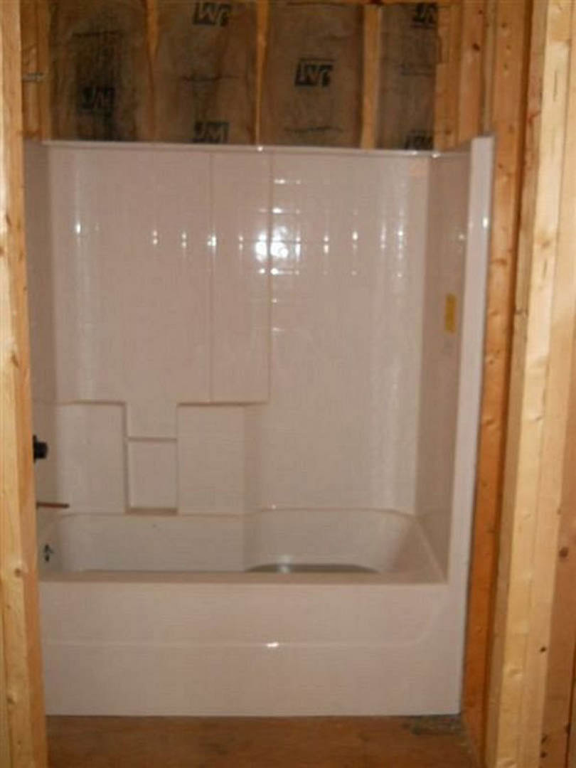 Freestanding white bathtub beside glass-enclosed shower, marble tile walls, wood plank flooring, chrome fixtures