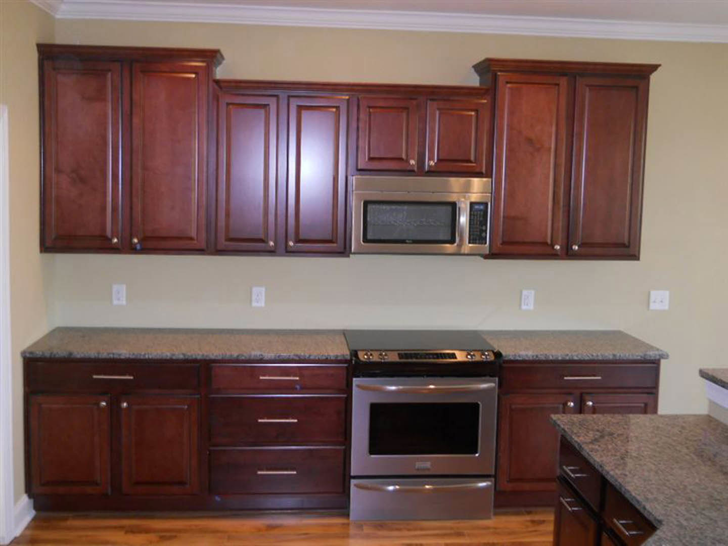 Kitchen featuring dark wood cabinets, granite countertops, stainless steel microwave and stove, multiple drawers, and upper cupboards