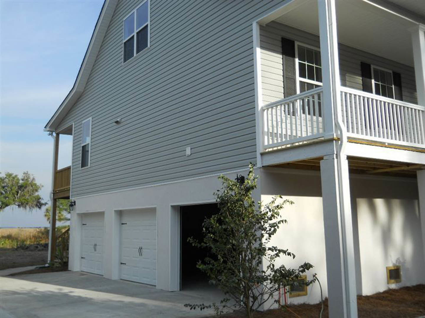 Two-story home with attached garage, upper balcony with metal railing, white siding, large windows, and a mature tree in the front yard.