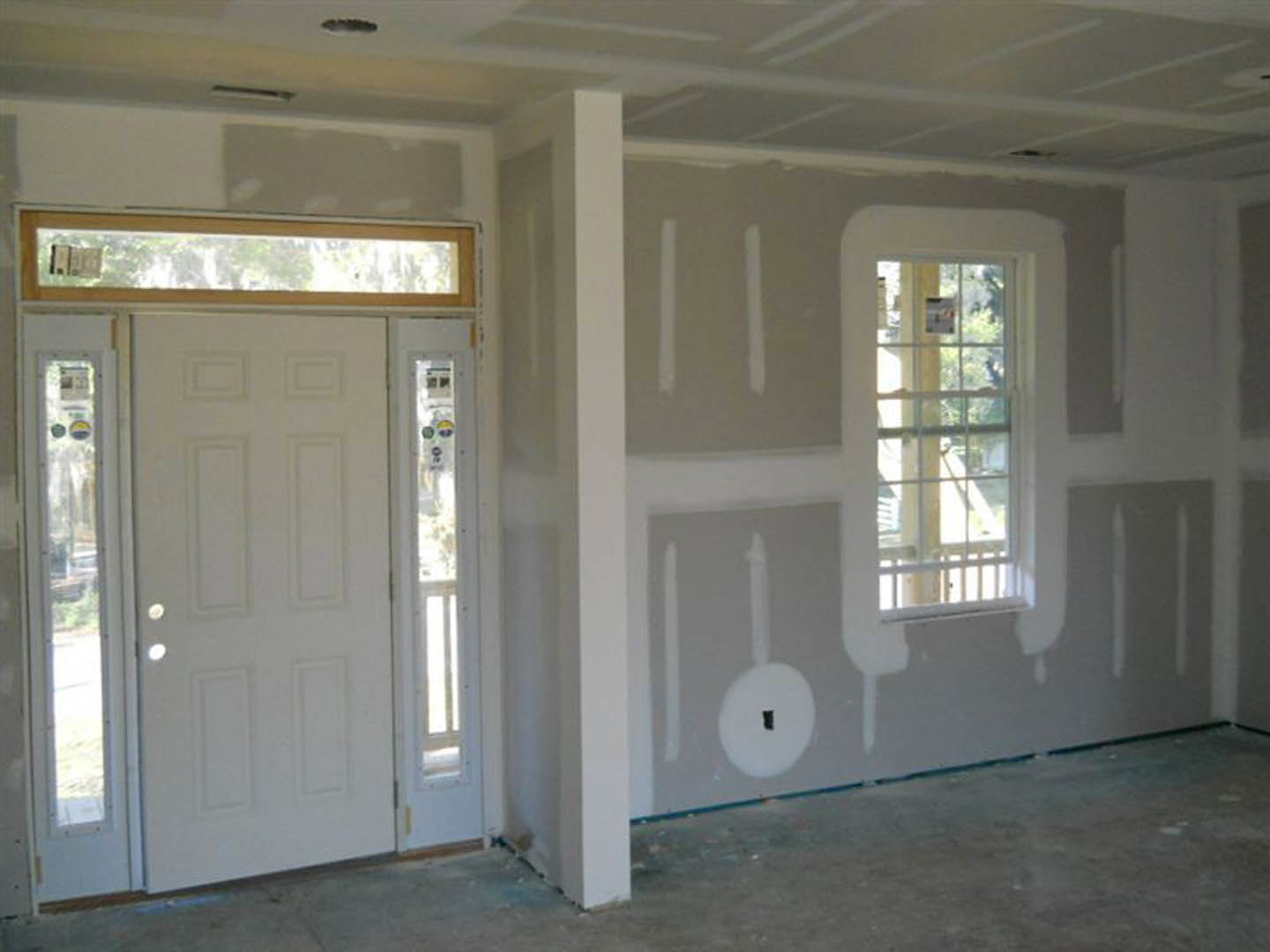White-walled room featuring a white door with glass panes, window offering outdoor view, light-colored flooring, and simple plaster molding.