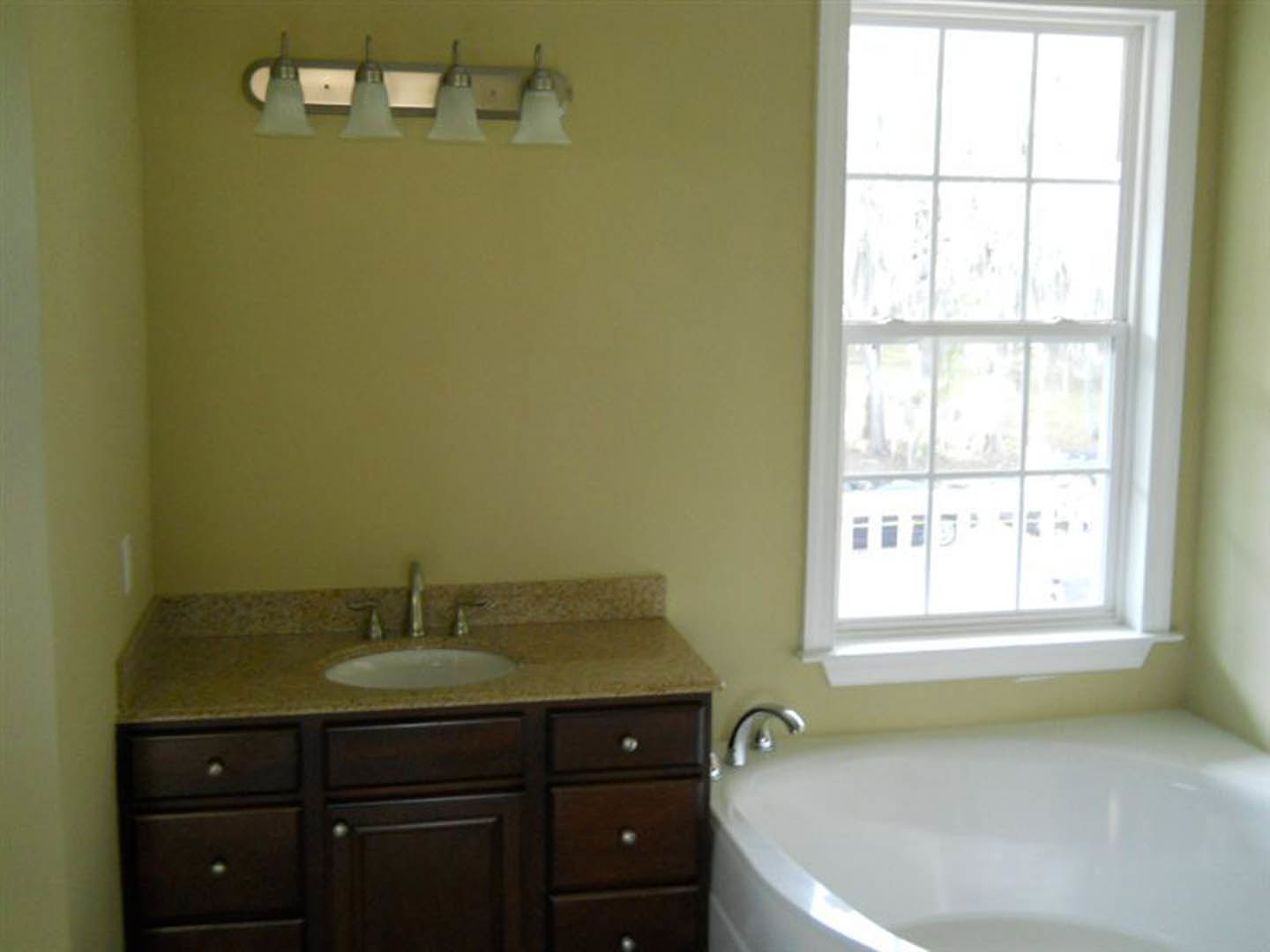 White freestanding bathtub beside a modern vanity with vessel sink, large wall mirror, gray tile flooring, and cabinetry under natural light from a window