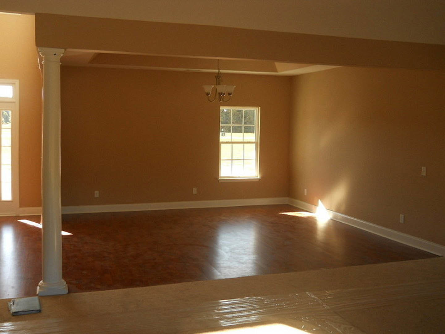 Spacious living room featuring shiny wood flooring, large window with outdoor view, white pillar, and smooth plaster walls