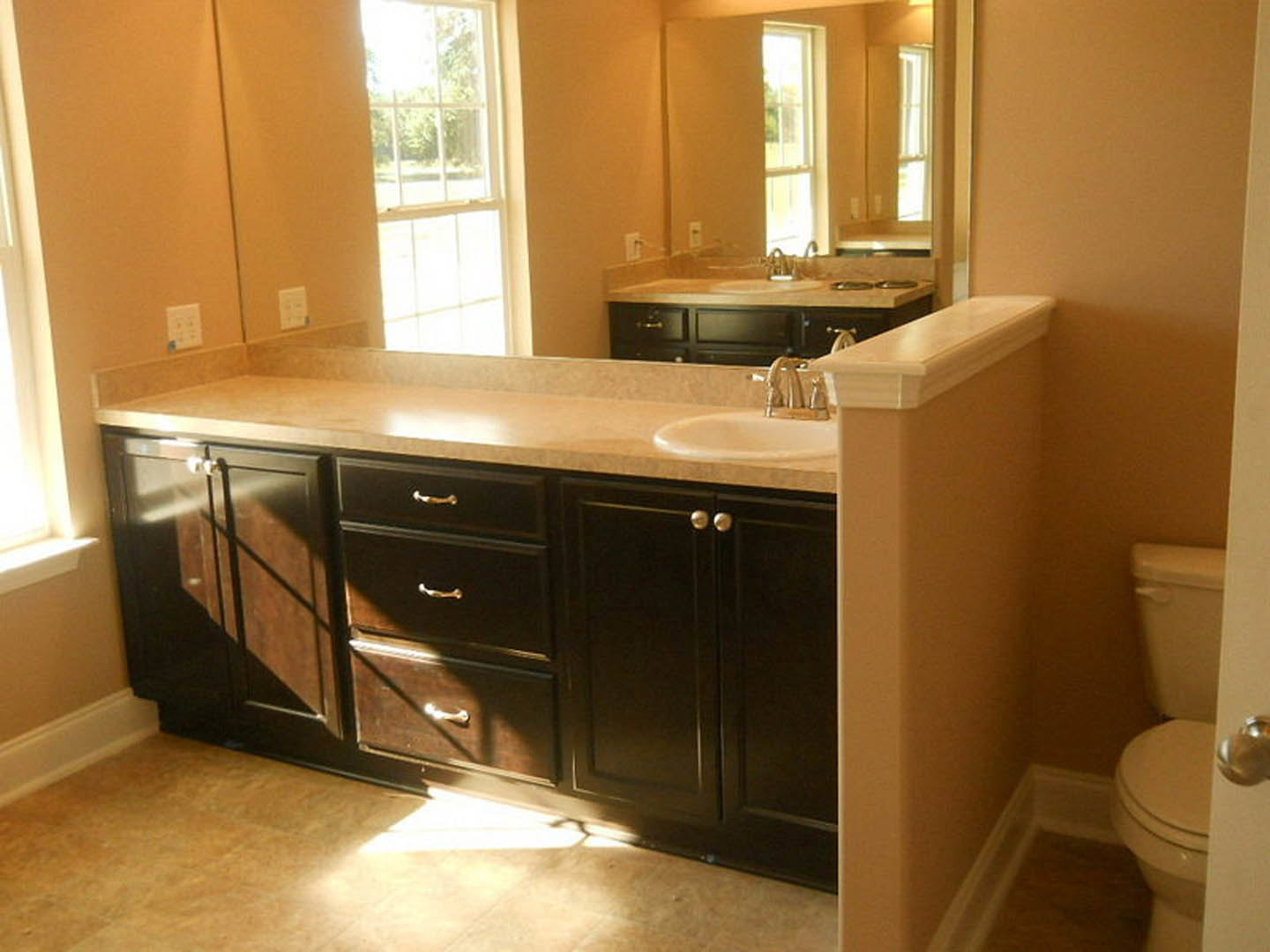 Bathroom with expansive mirror above white countertop, light tile backsplash, modern cabinetry, chrome faucet, and visible wall outlet with blue sticker.