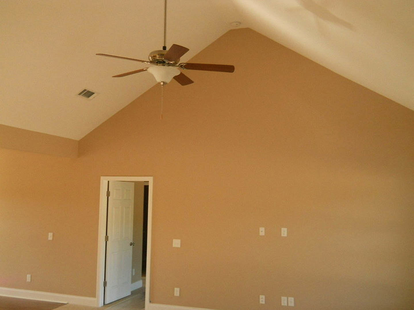 Ceiling fan with integrated light fixture mounted on white plaster ceiling, white door with silver knob, neutral walls, crown molding, and glass container holding brown object on