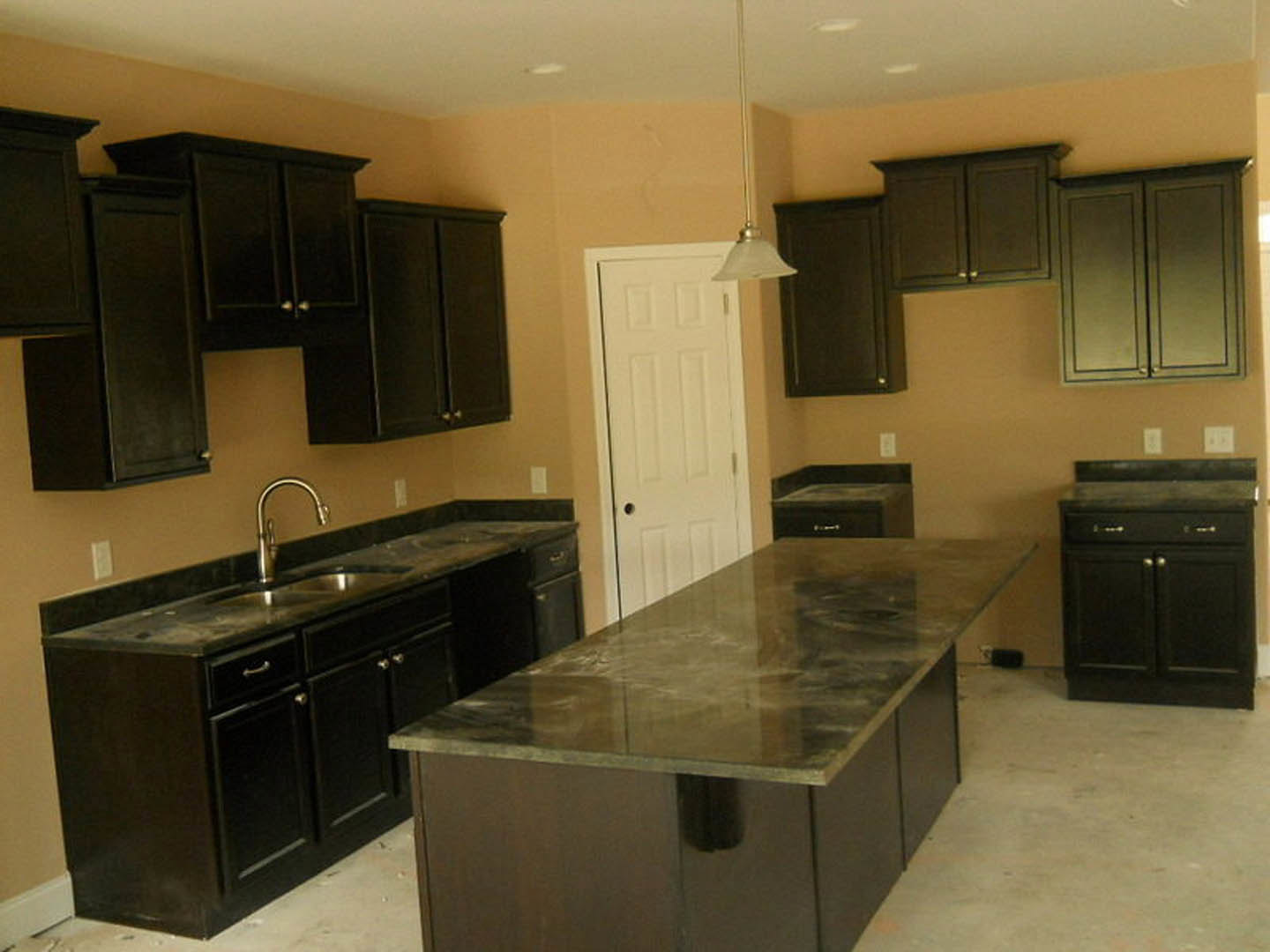 Kitchen with dark wood cabinets, marble island countertop, stainless steel faucet, white door with black handle, tile backsplash, and integrated appliances