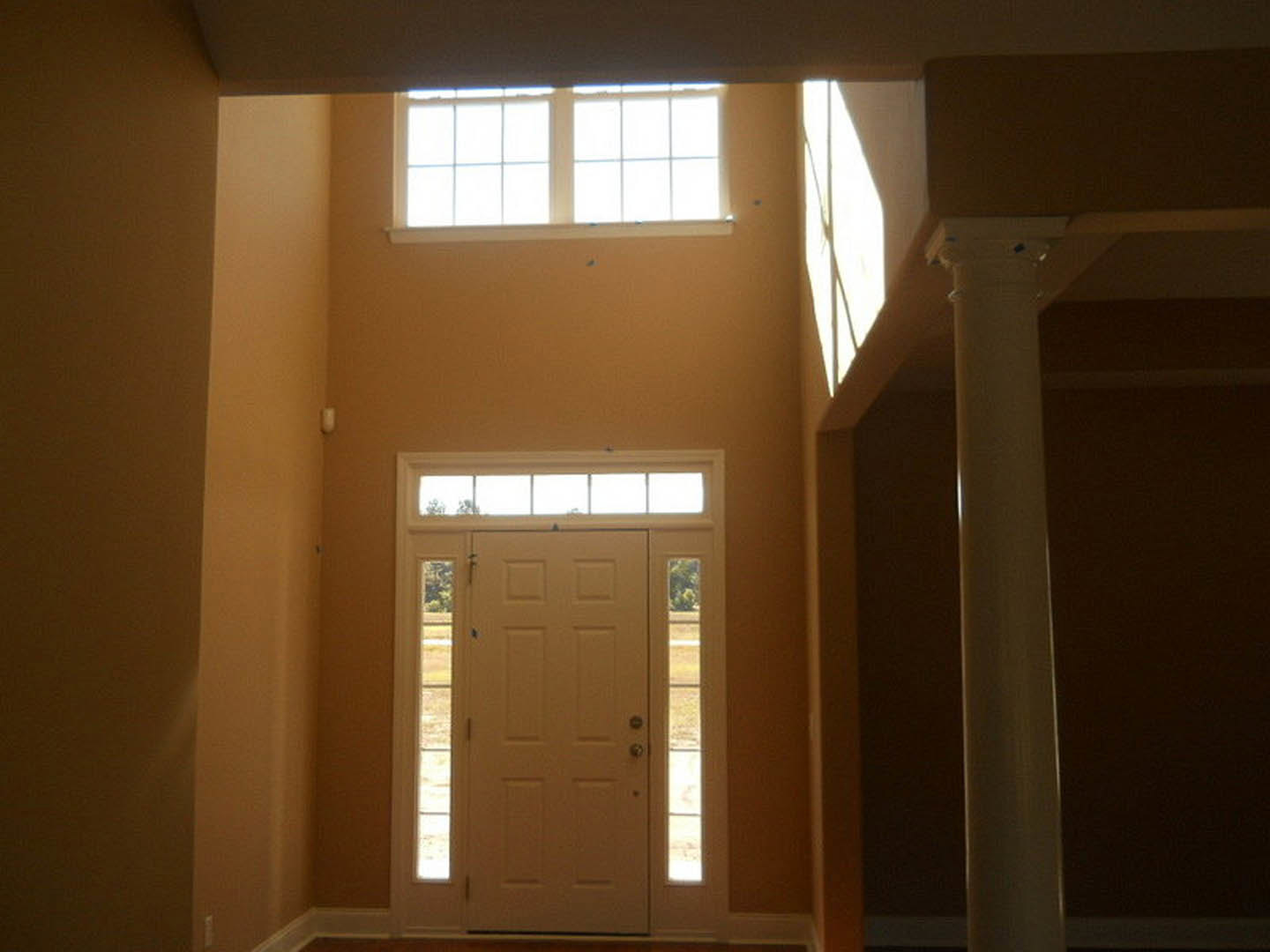White paneled door with glass window inserts, surrounded by white molding and adjacent wall, illuminated by natural daylight.