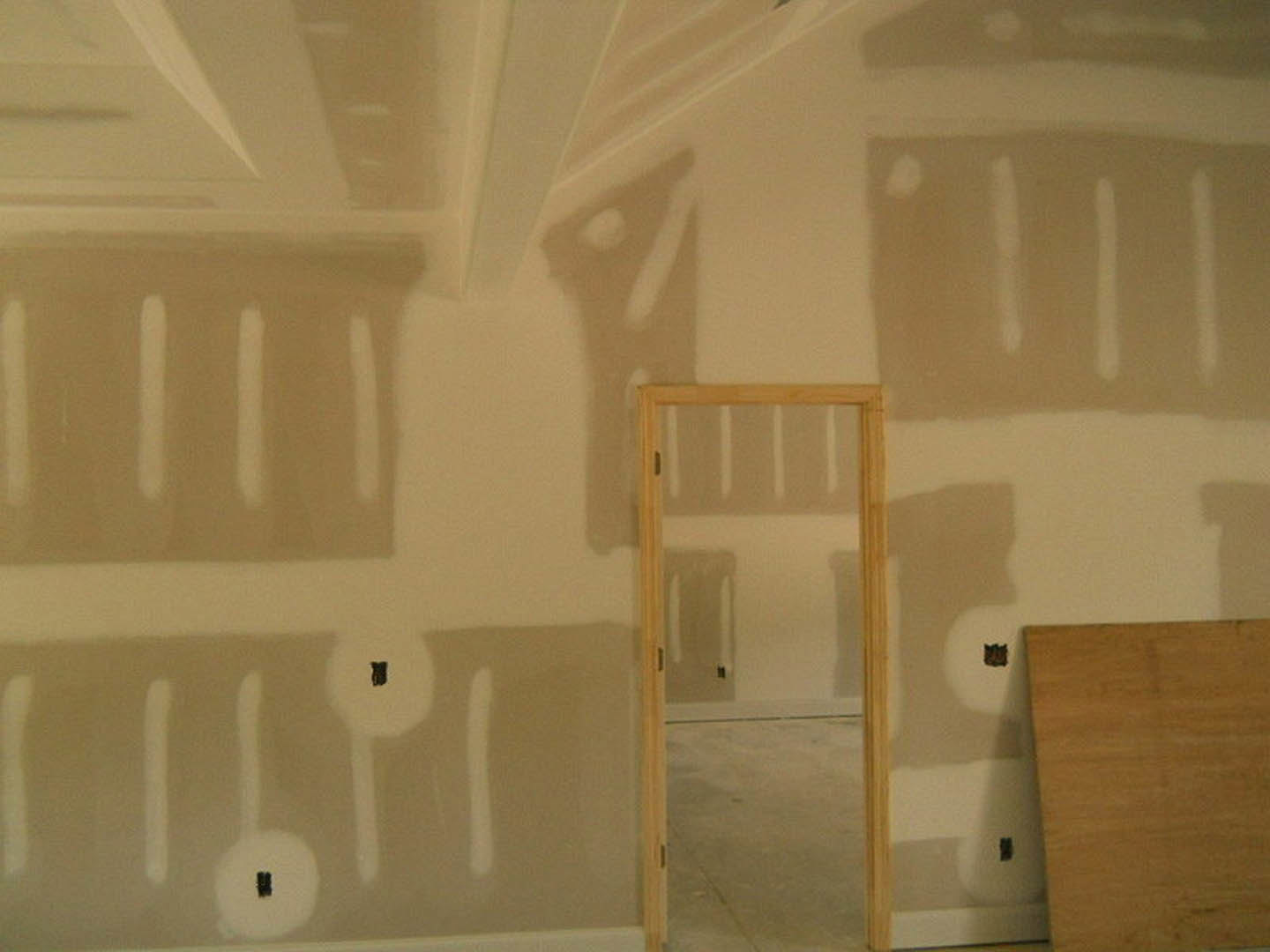 White-painted drywall wall with wood door frame, subtle shadow cast on wall, light plywood floor, and smooth plaster ceiling in a modern interior room.