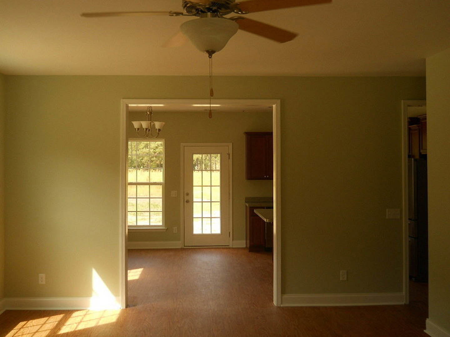Living room with light-colored walls, white framed windows, glass-paneled white door, ceiling fan with dark blades, wood flooring, and crown molding.