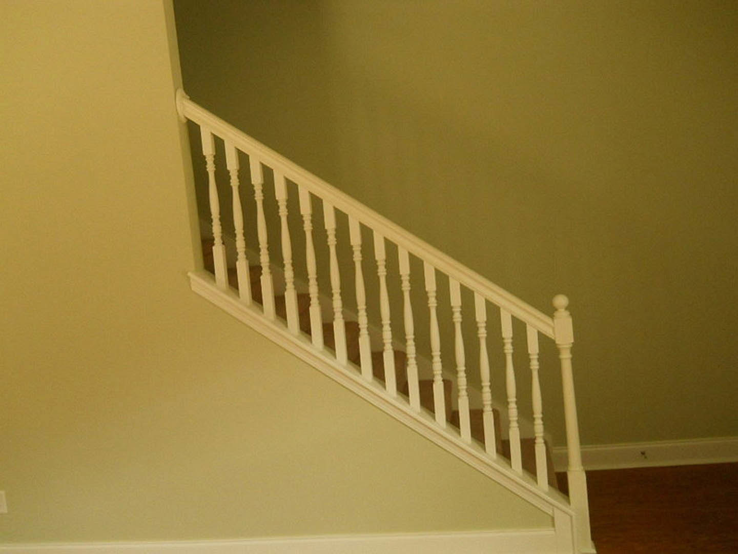 White-painted staircase with matching railing, wooden floor, plaster walls, and baluster details in a bright interior.