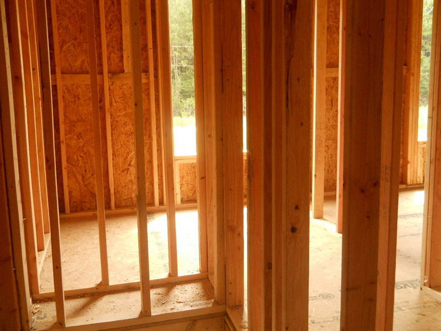 Exposed wood ceiling beams, large window with sunlight streaming in, unfinished wooden floor and framing in a residential room
