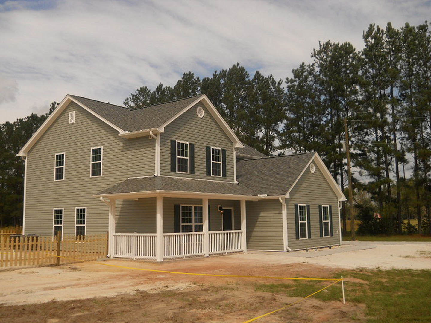 Two-story home with white porch railing, multi-pane windows, and landscaped yard with trees under a partly cloudy sky
