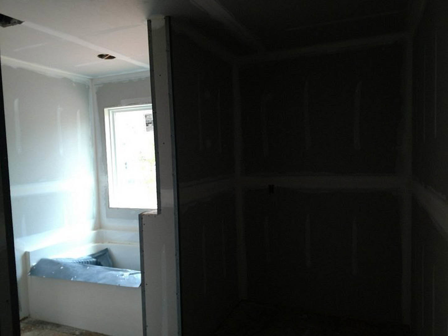 Freestanding white bathtub beneath large window, light gray plaster walls, wood floor, minimal decor