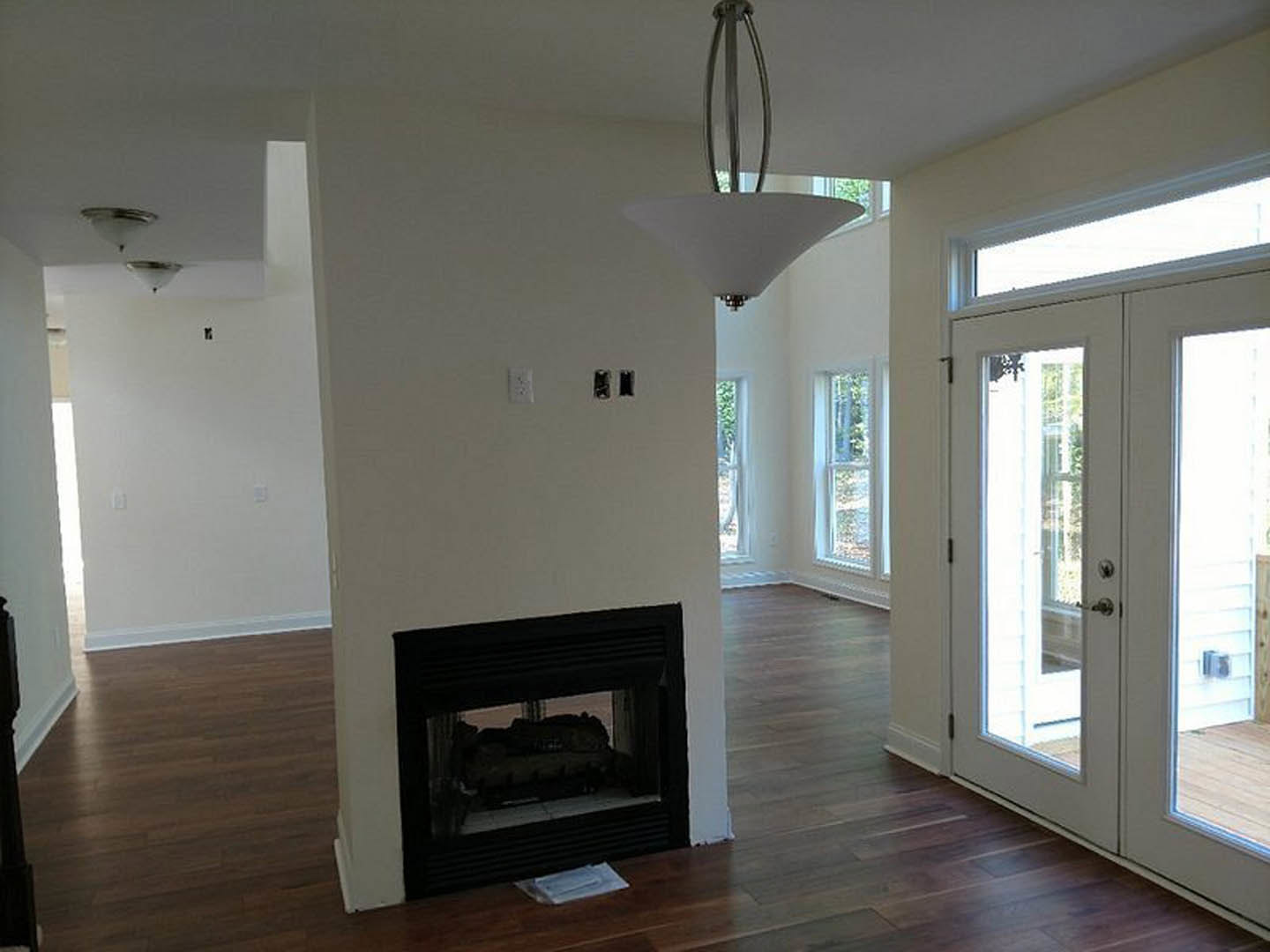 Modern living room with glass-door fireplace set in a white wall, wood flooring, and minimalist decor