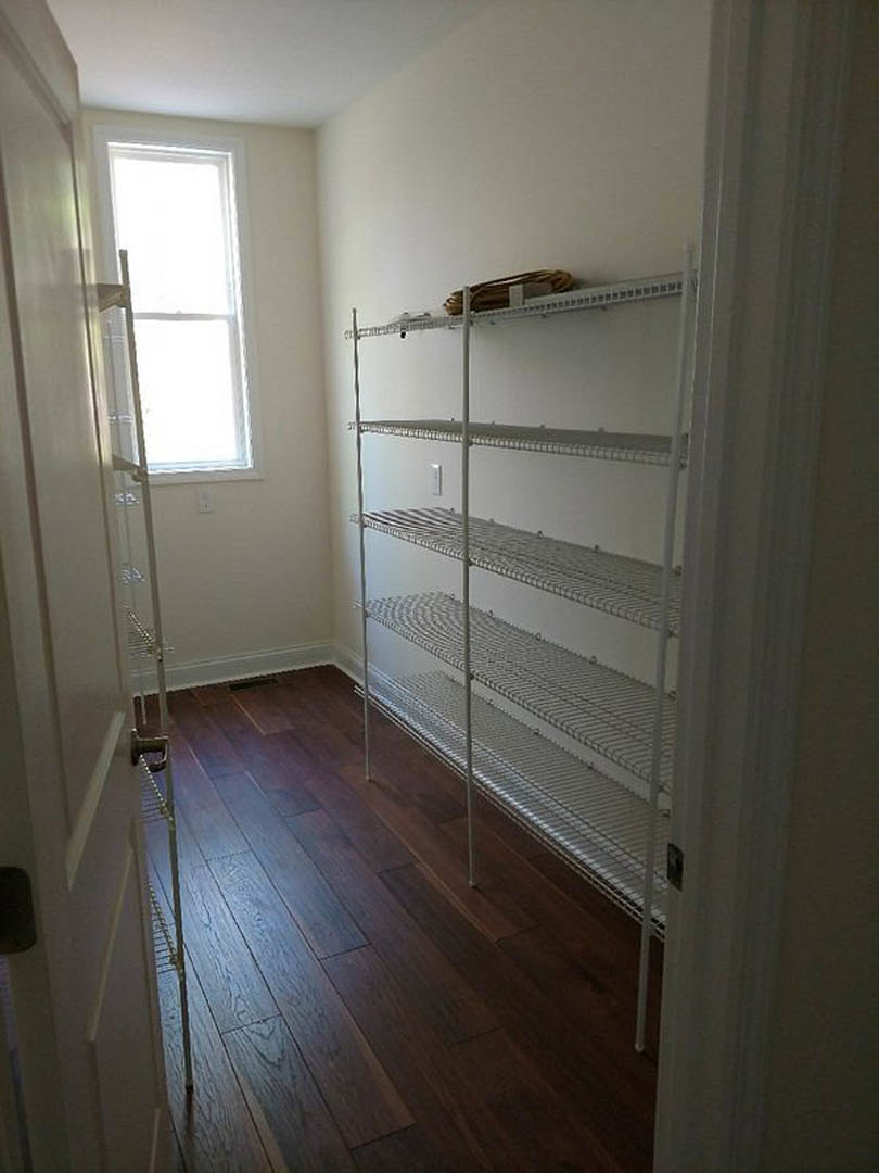 Wood flooring, white built-in shelves along wall, large window allowing natural light, neutral plaster walls, minimalist cabinetry.