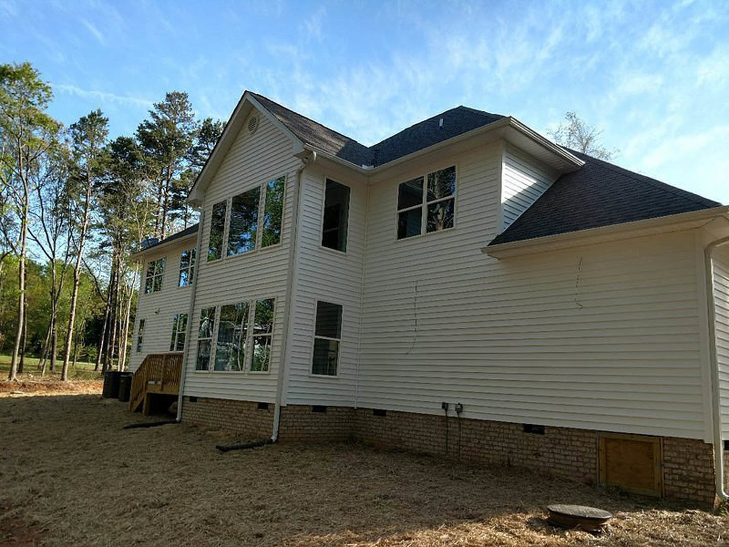 White house with horizontal siding, brick accent wall, wooden deck, grassy yard, and mature trees in the background