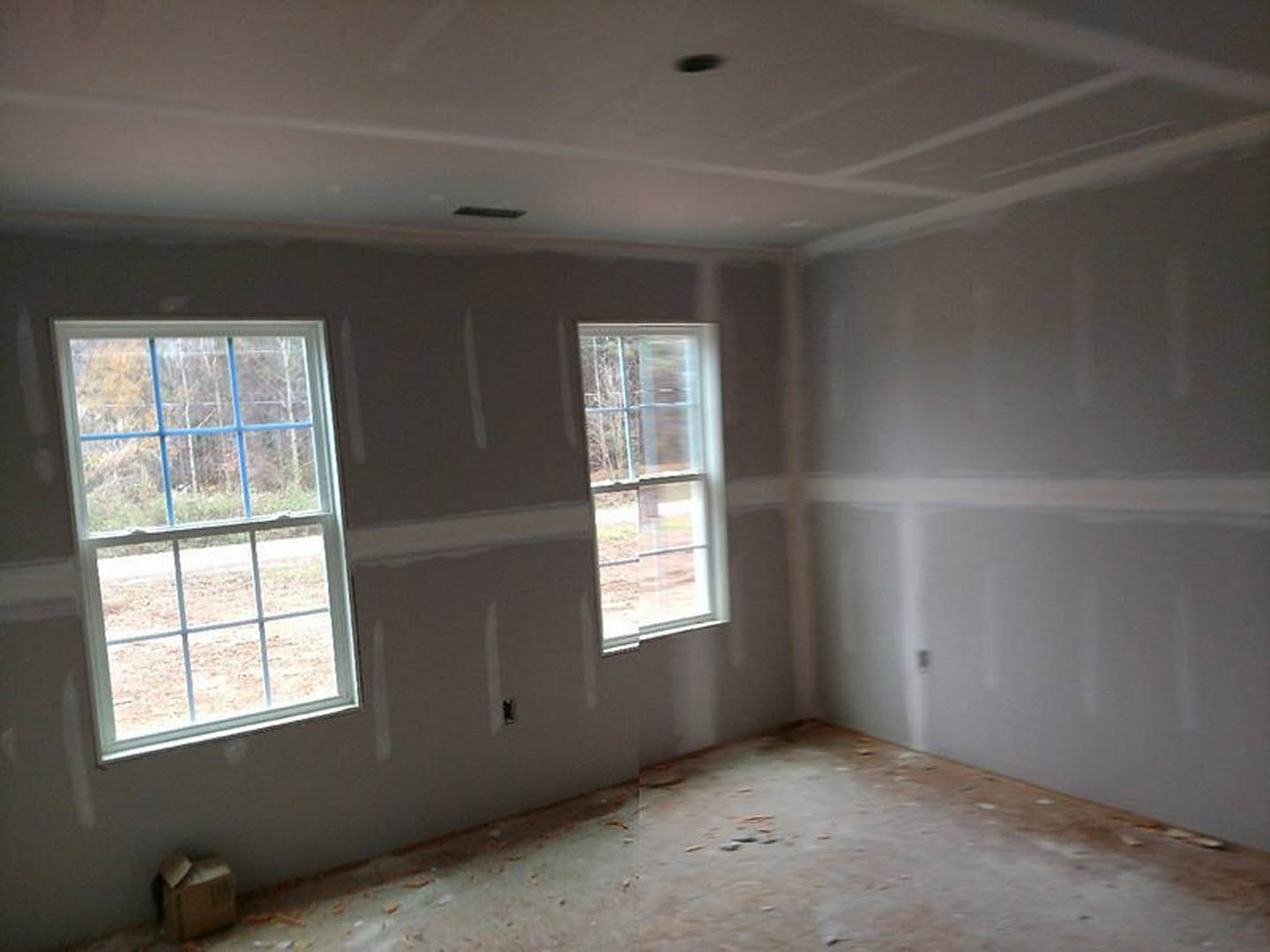 Bright room with large windows, white plaster walls, and light-colored flooring; daylight streams in, highlighting modern interior finishes.