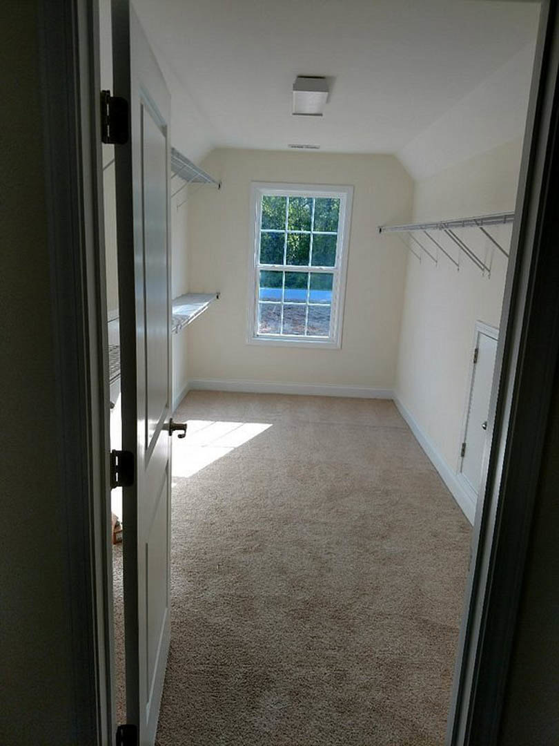 Walk-in closet with built-in white shelves, metal hanging rods, and a window overlooking trees, illuminated by natural light