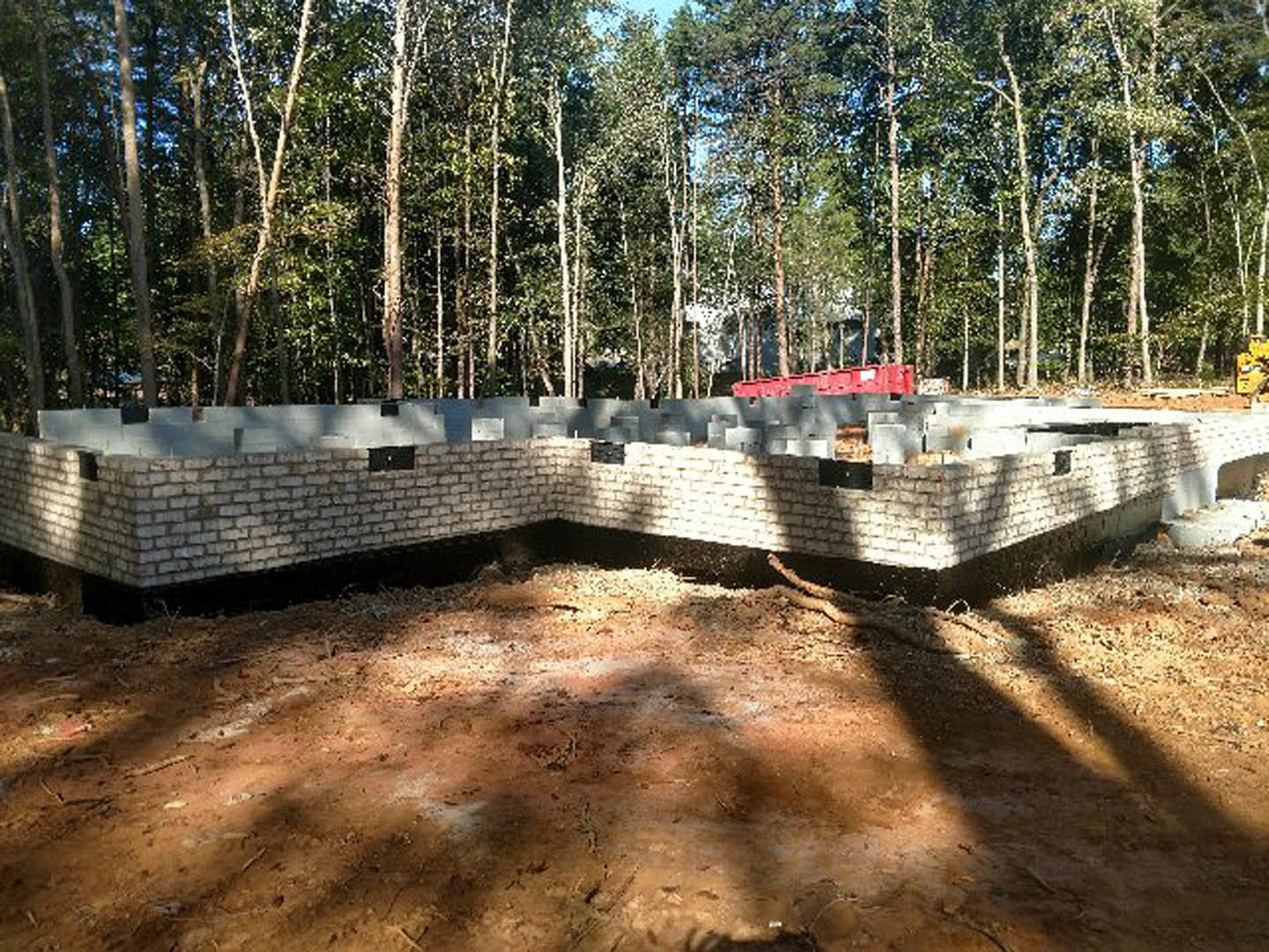 Brick foundation surrounded by tall trees in a forest, exposed brick wall with an opening, natural ground and sky visible
