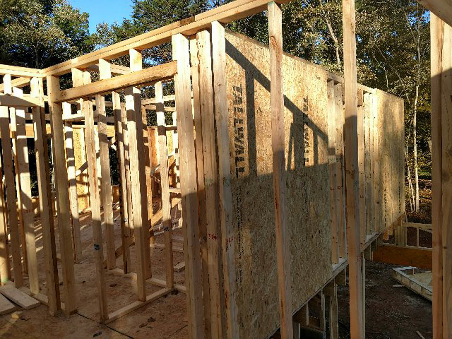 Wood-framed exterior walls and beams of a custom home under construction, surrounded by trees and open sky