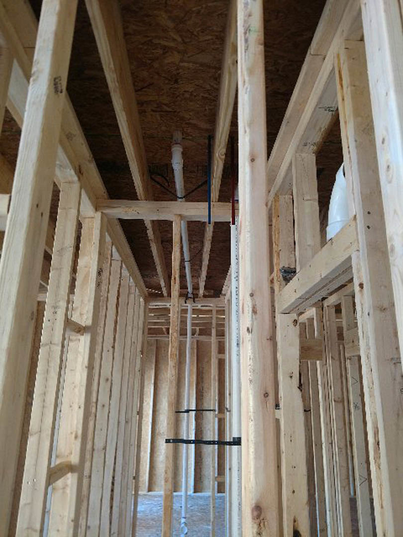 Exposed wood framing with vertical beams, metal brackets, and insulation visible inside unfinished residential construction