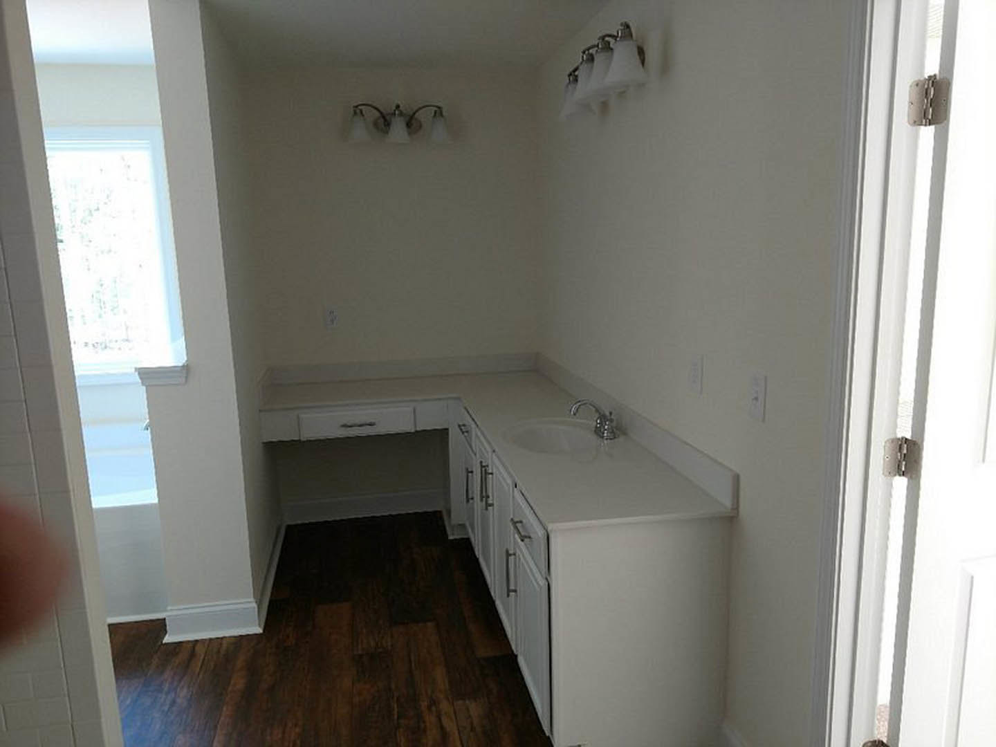 Bathroom with white sink, dark wood flooring, white baseboards, wall-mounted lights, doorway with window, and plaster walls