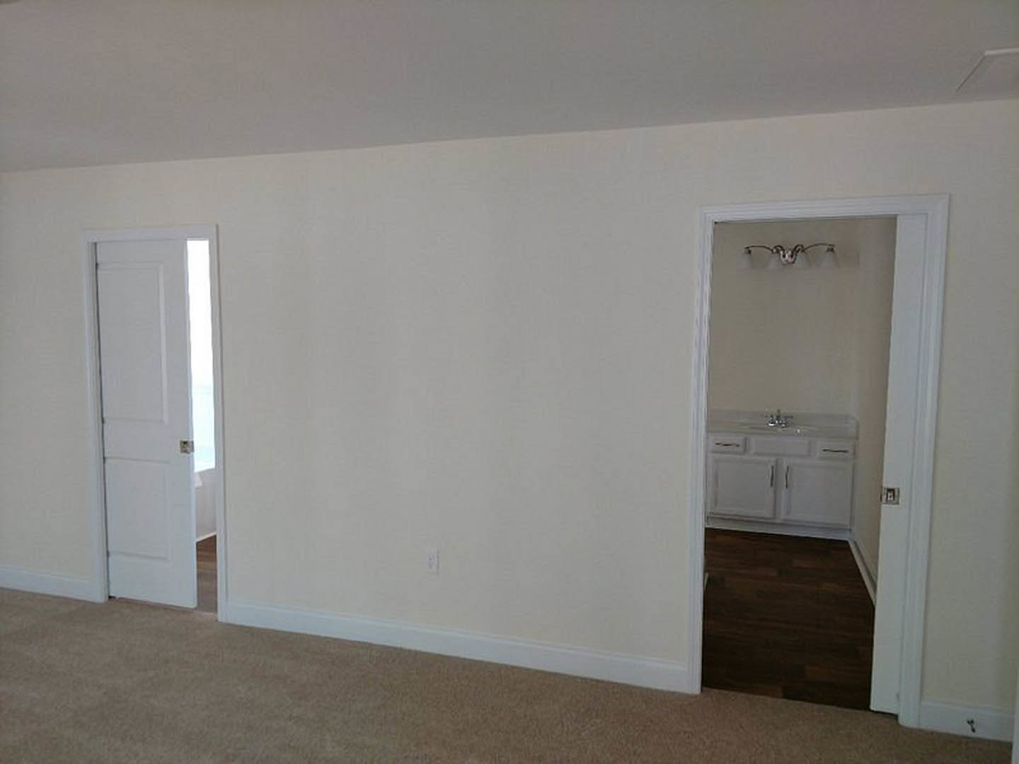 Dark wood floor with white trim, white walls, white bathroom sink with silver handles, close-up of white door in a room