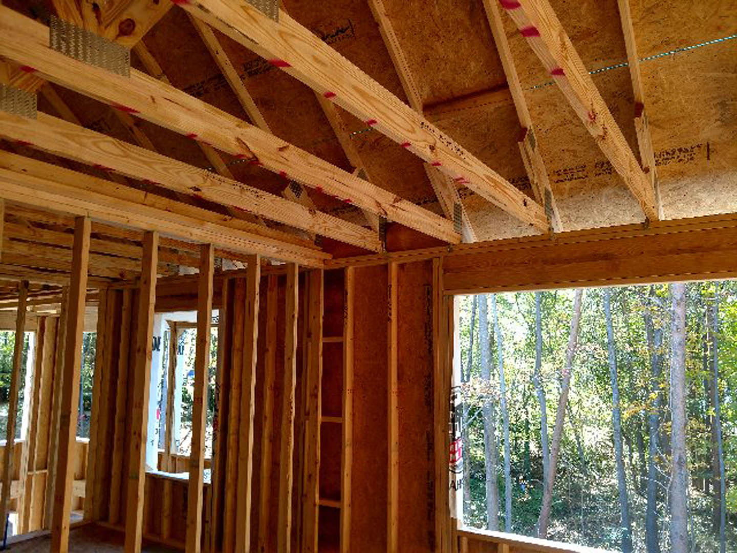 Exposed wooden beams and framing inside a partially constructed house with unfinished plank walls and ceiling