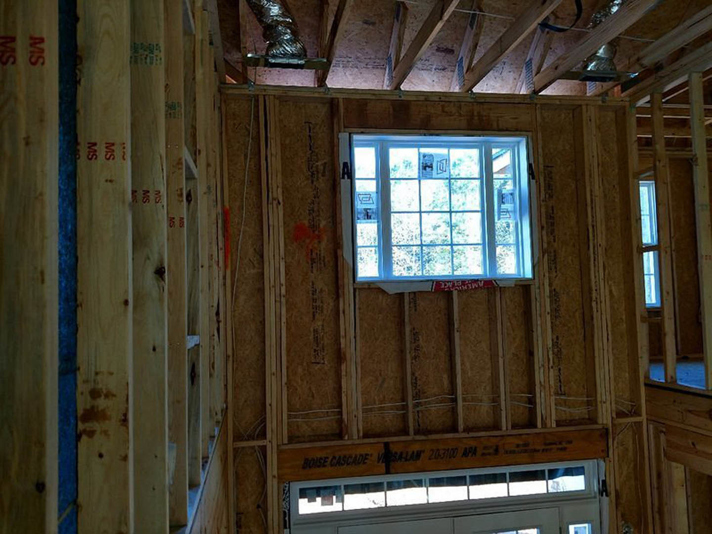 Bright room featuring a white-framed window, wooden beams, and plank walls; door visible beside window, building insulation partially exposed.