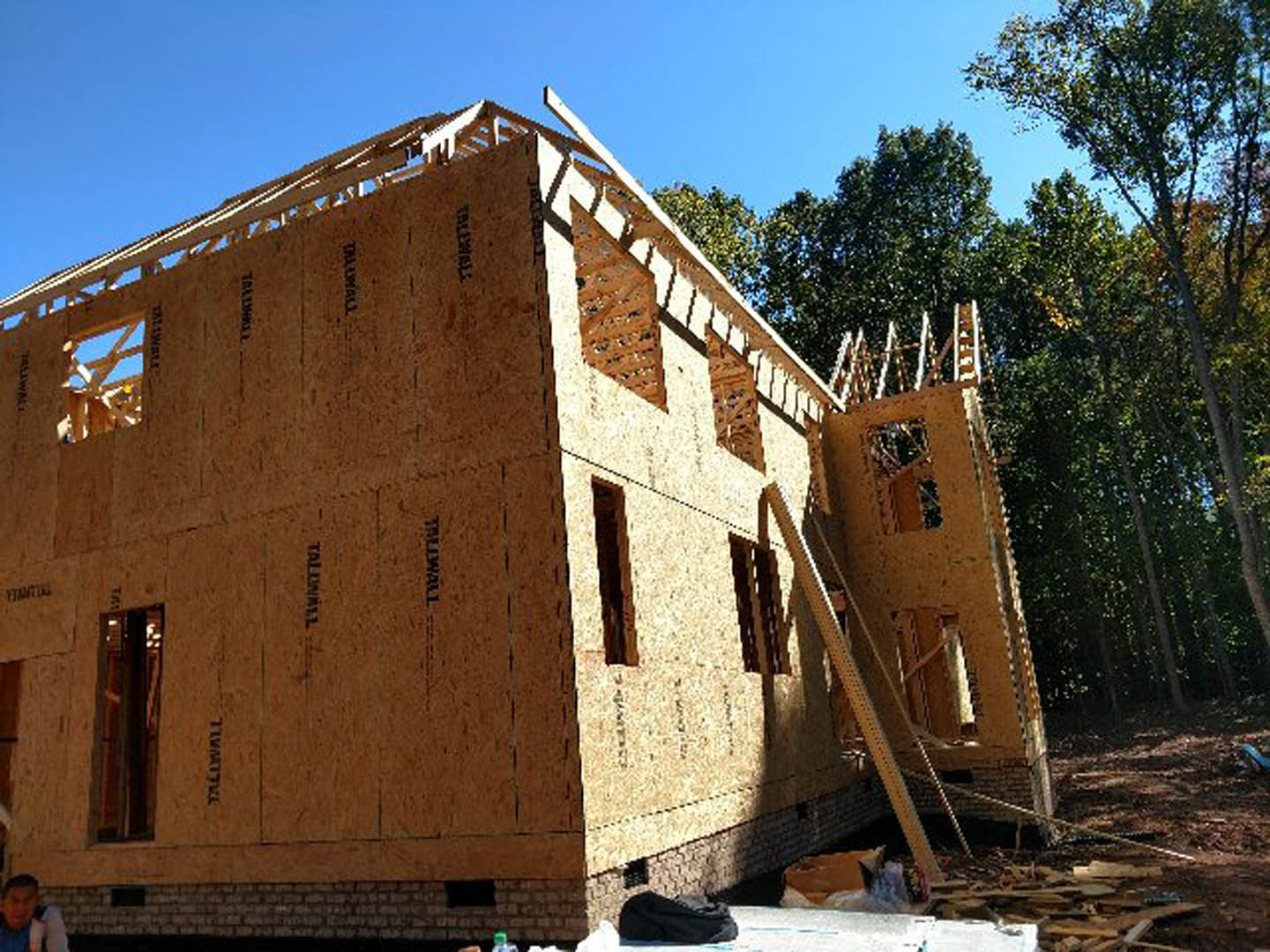 Brick exterior home under construction with exposed framing, surrounded by mature trees and open sky in the background