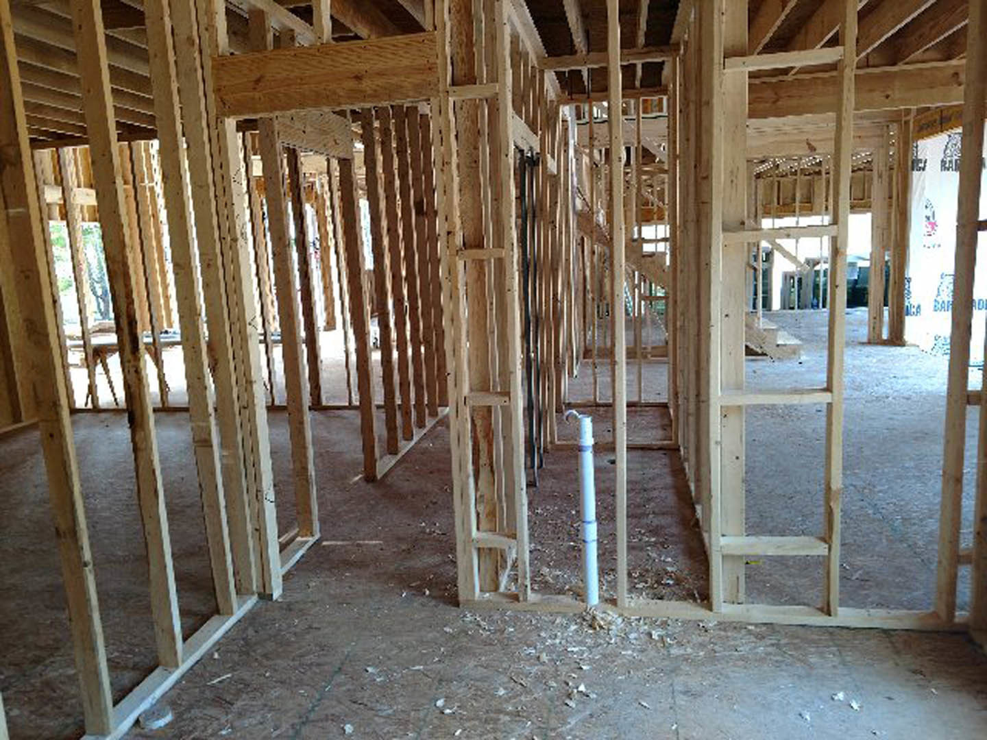 Exposed wooden framing and beams inside a house under construction, white pipe resting on unfinished floor